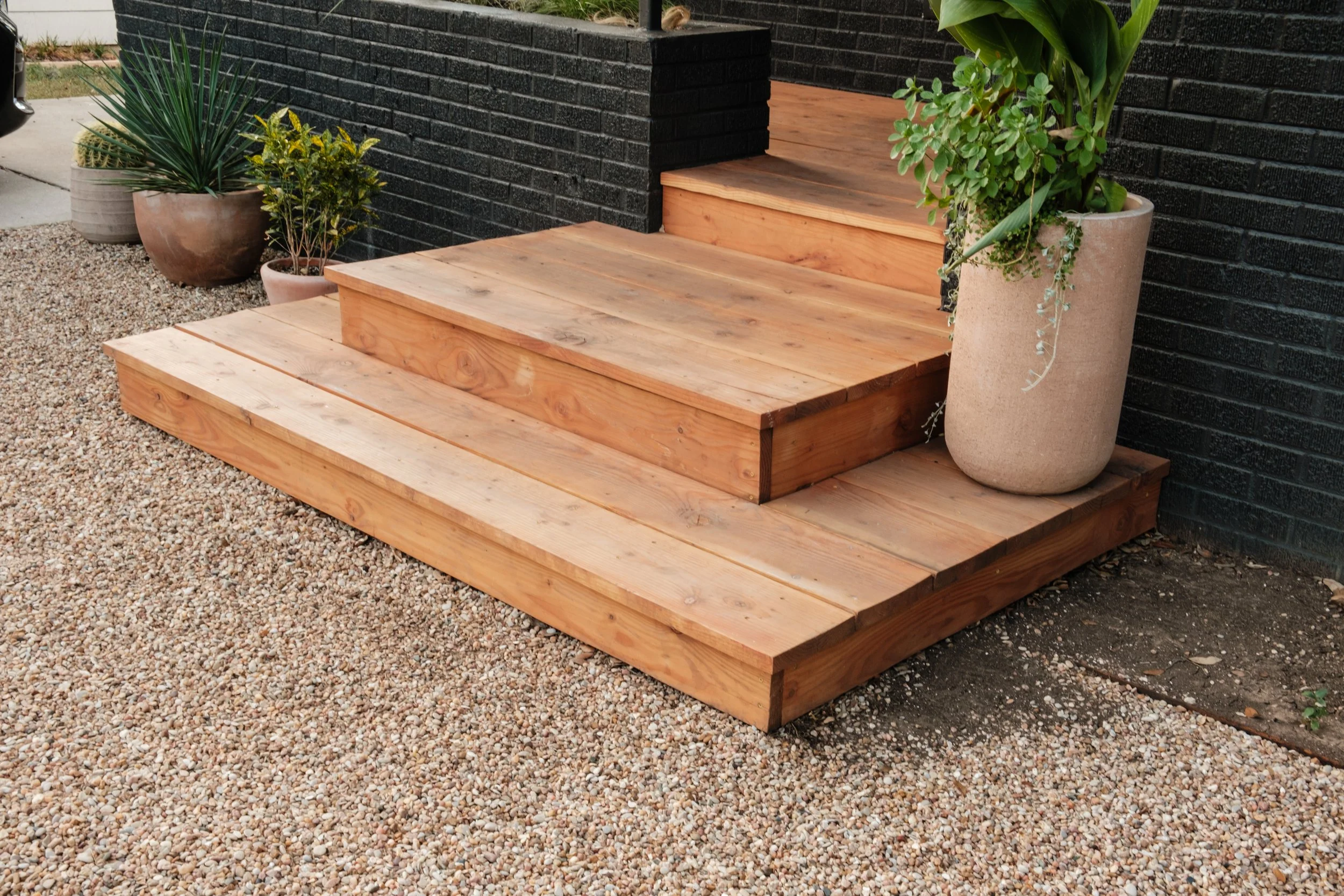 Wooden steps leading to a black brick porch, with potted plants on either side.