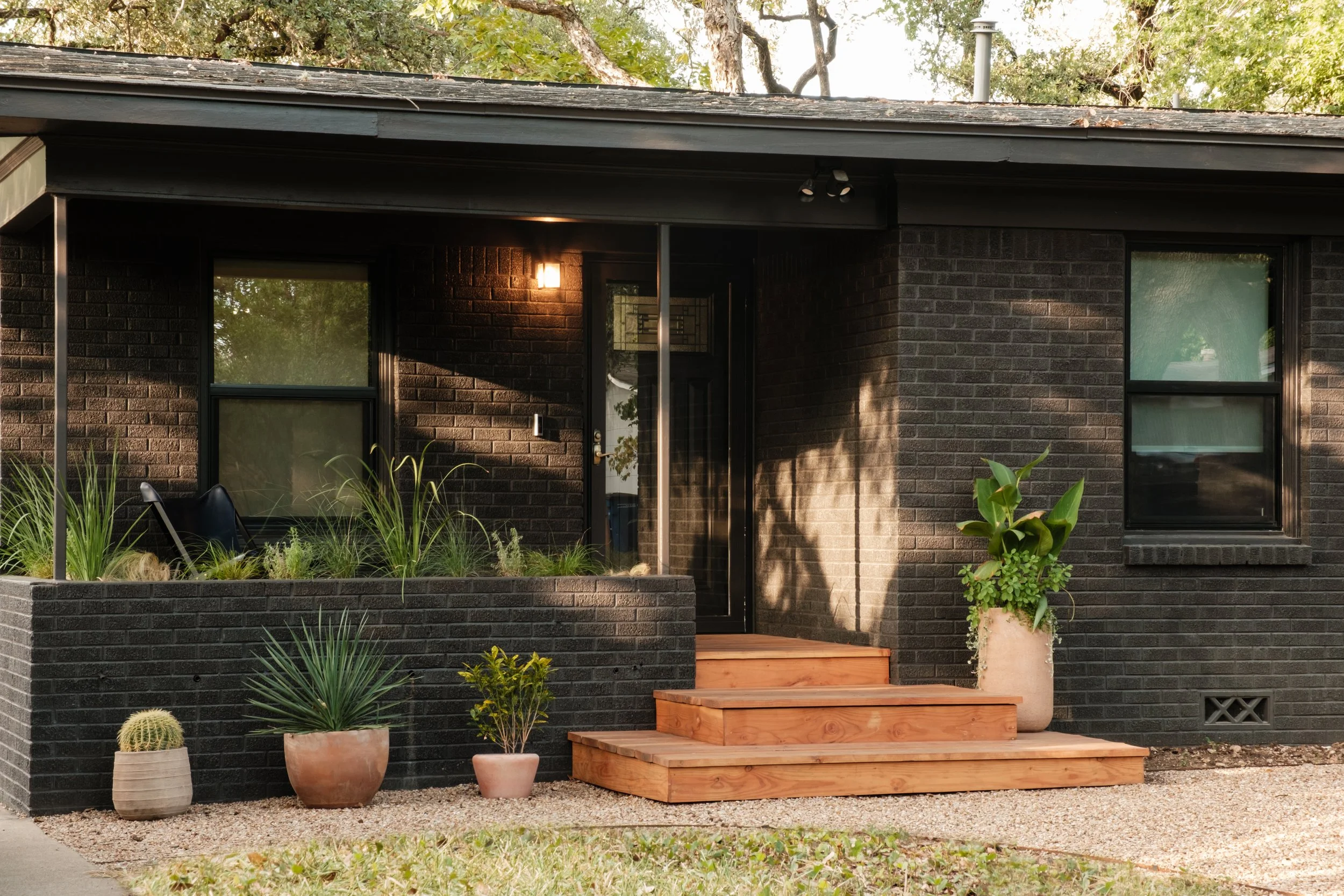Black brick house with front porch, potted plants, and wooden stairs leading to the entrance.