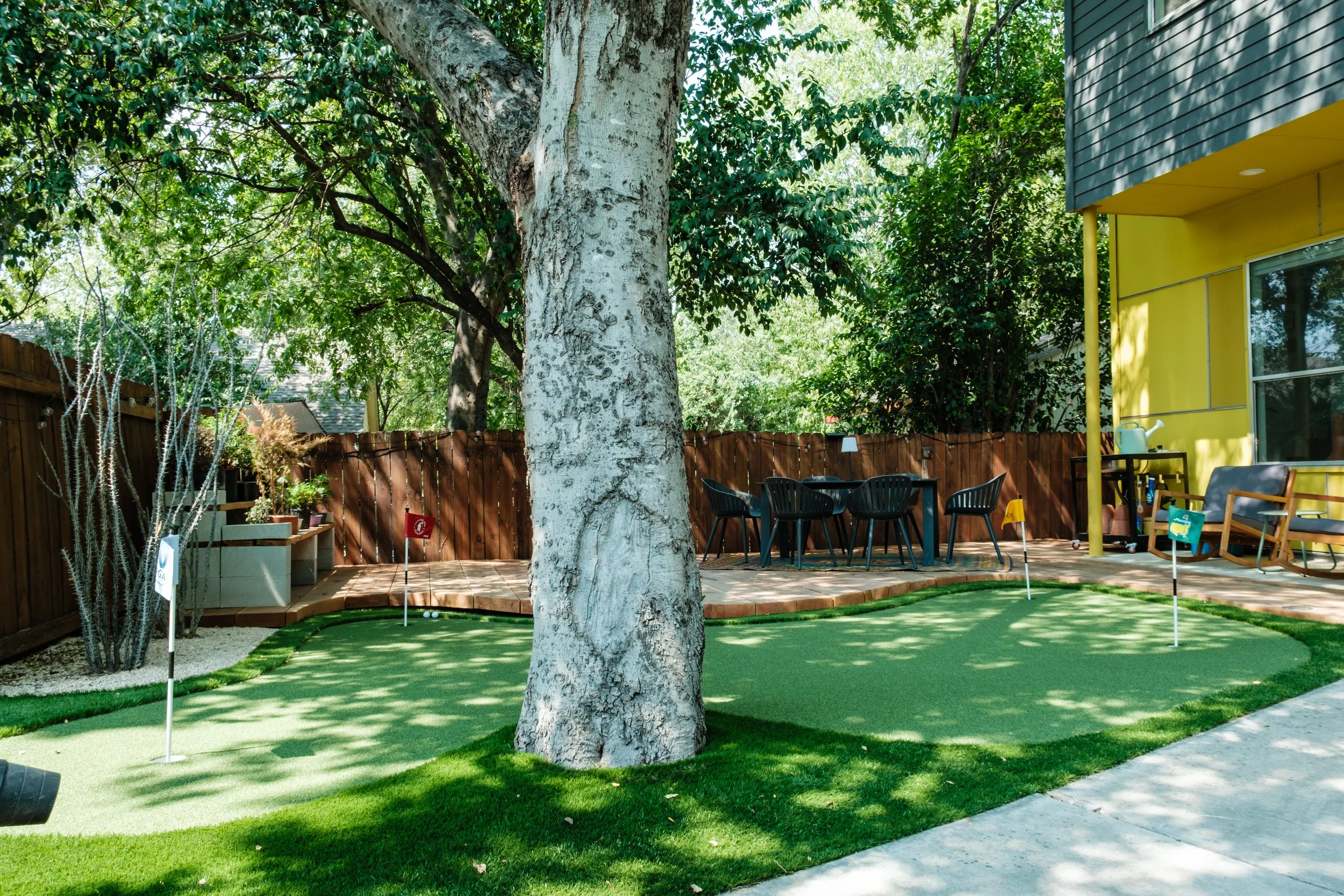 Backyard with a large tree, patio area, outdoor furniture, and a small golf putting green with flags.