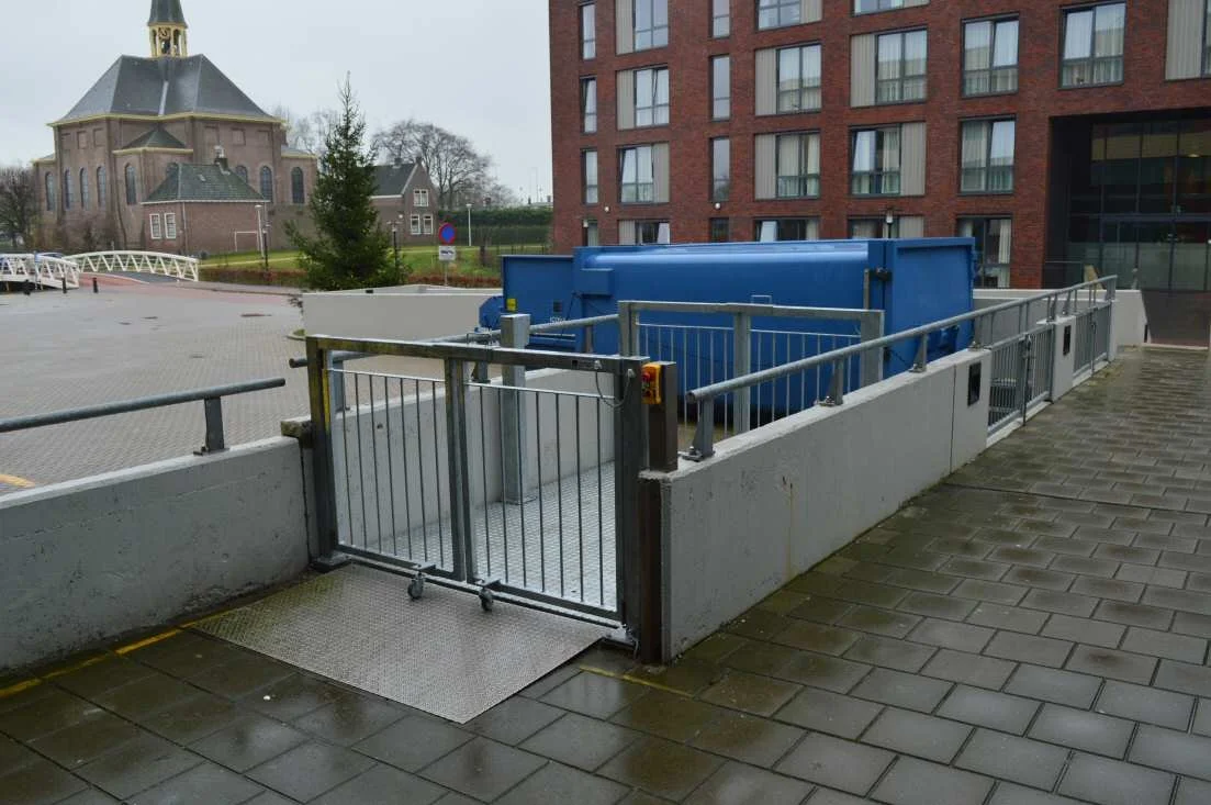 A small gated entrance with metal railings leading to an underground or basement area, next to a modern multi-story apartment building.