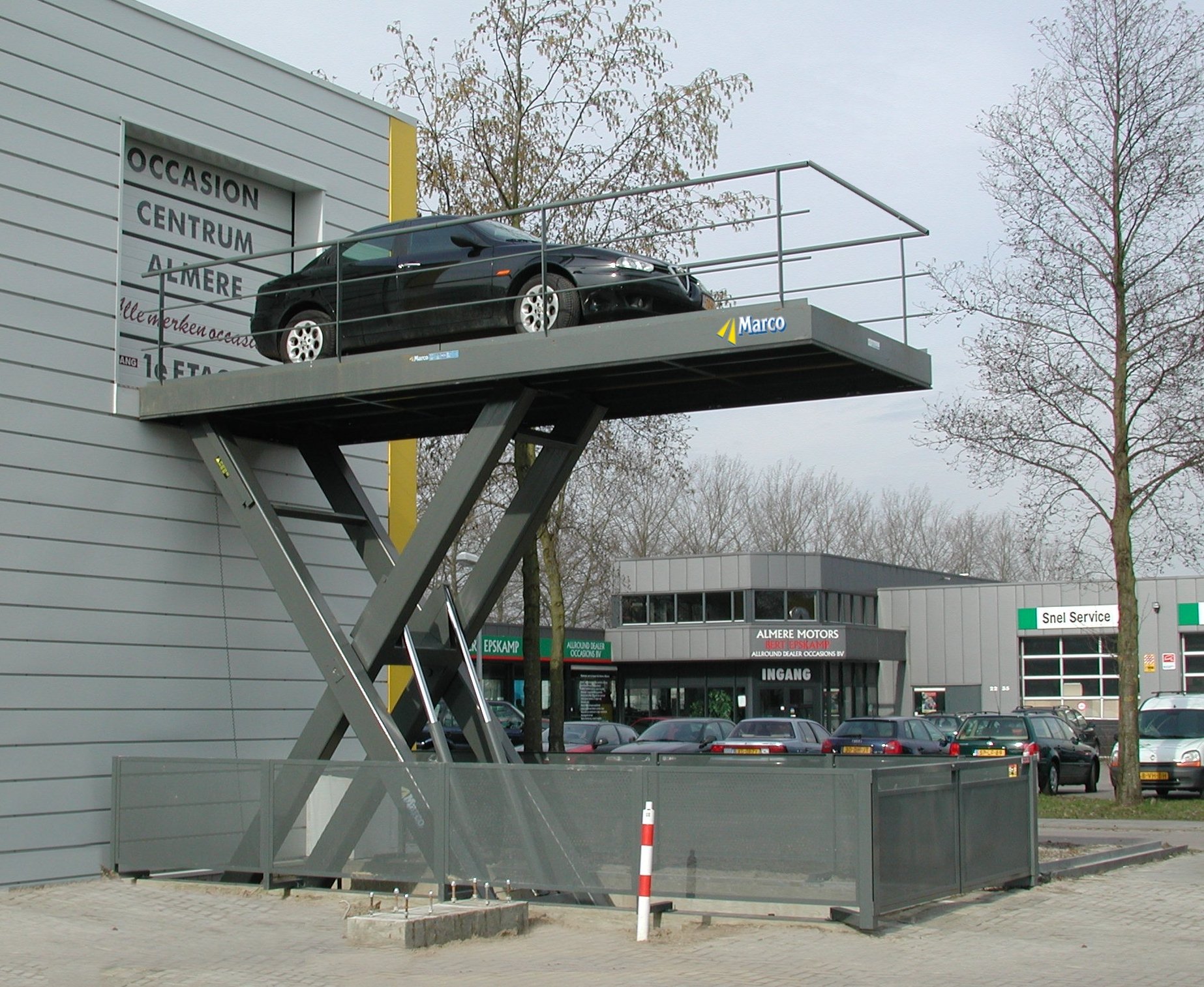 A car on a raised platform outside an auto dealership, with the platform resembling a car lift.
