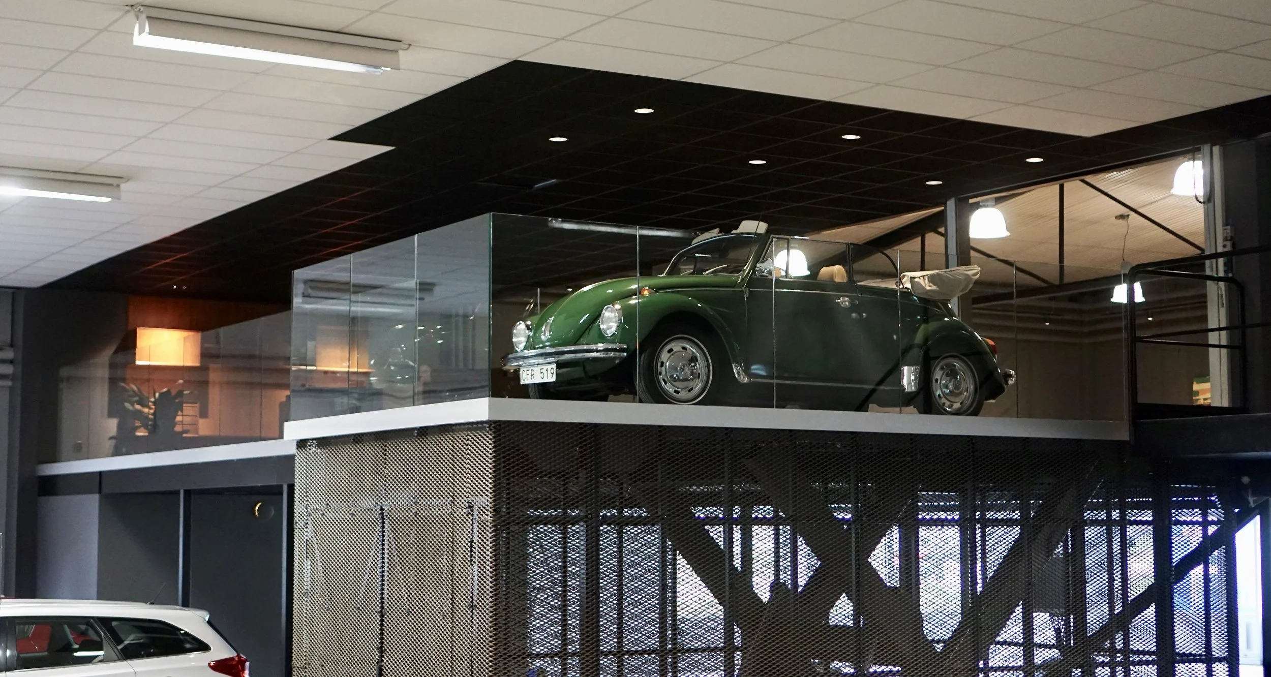 A vintage green convertible car displayed on an upper level inside a modern building with glass walls and metal structures.