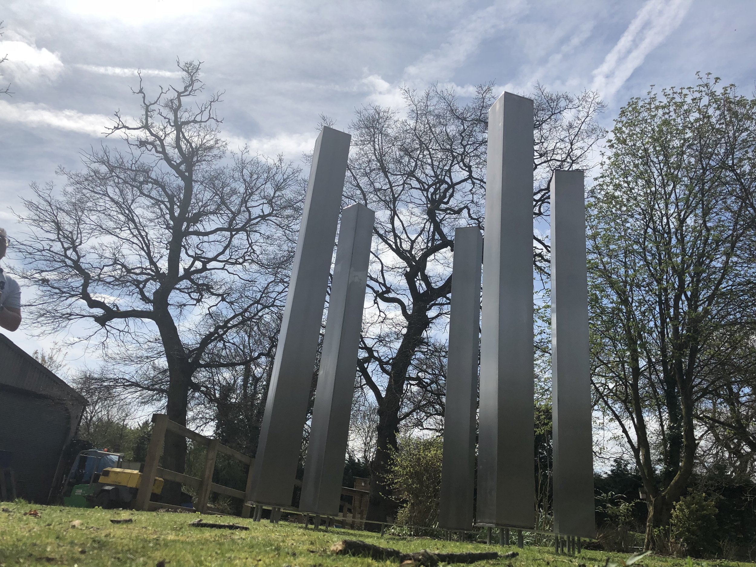 Tall metallic sculptures on grassy lawn with leafless trees and blue sky in the background.