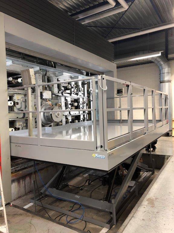 Industrial machinery with a secure railing and a platform in an indoor industrial or manufacturing setting.