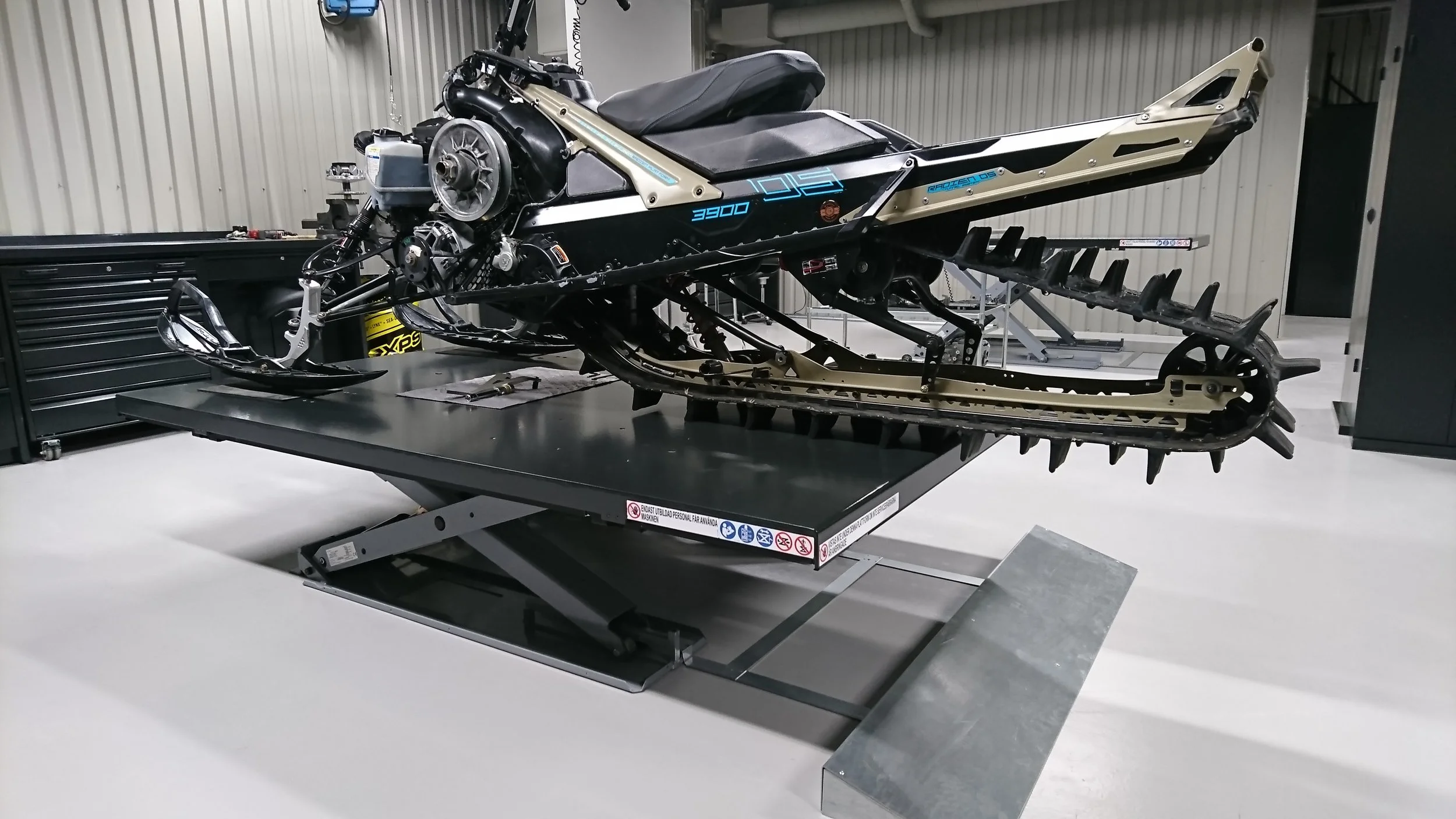 Snowmobile with track and engine, placed on an adjustable lift in a workshop.