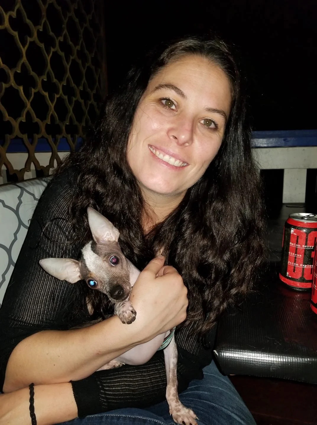 A woman with dark wavy hair smiling while holding a small dog smiling because she is happy she hired a professional organizer and decluttering specialist in her home in Kennesaw, Georgia. 