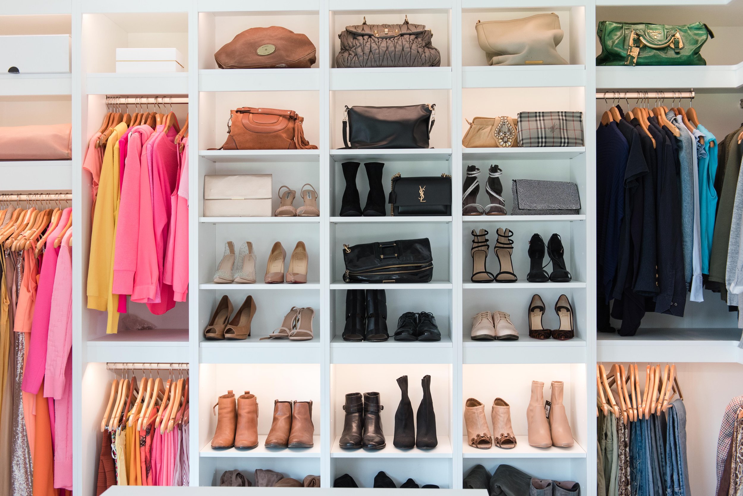 A closet with shelves of handbags, shoes, and hanging clothes including pink, yellow, and black garments.