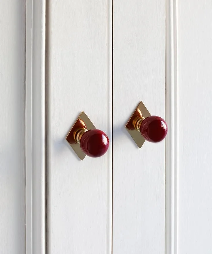 Close-up of a white cabinet with two red doorknobs.