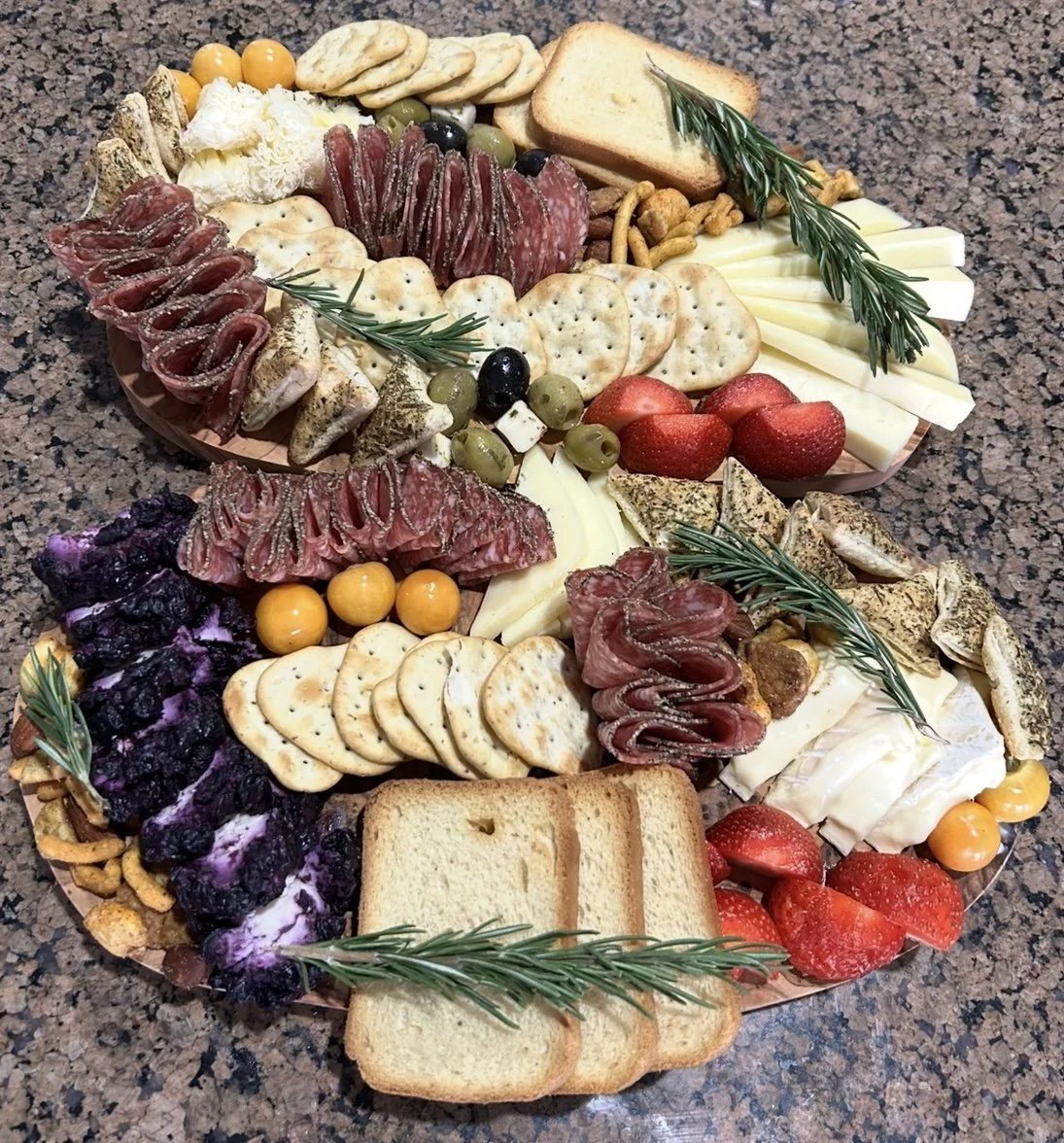 A large cheese, fruit, and cracker platter with assorted meats, cheeses, strawberries, blueberries, grapes, crackers, bread slices, and garnished with fresh rosemary.