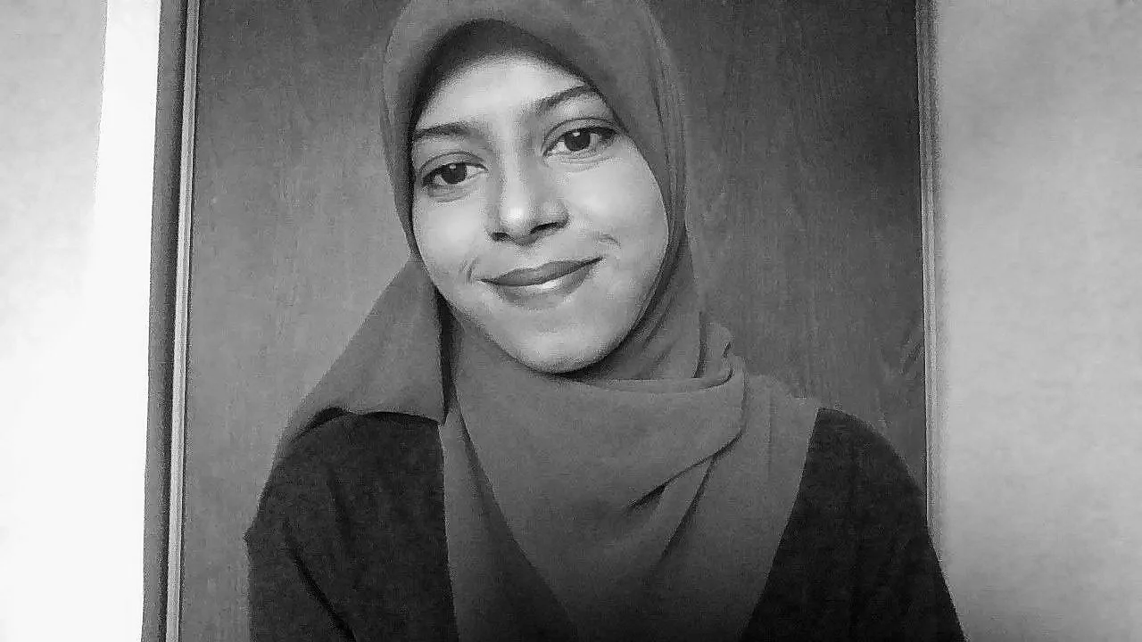 Black and white photograph of a woman wearing a hijab, smiling, and looking at the camera.