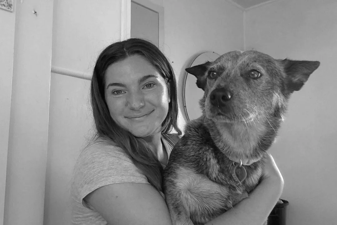 A woman holding a dog in black-and-white photo, smiling, indoors with door and mirror in background.