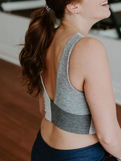 Side view of a woman with brown hair in a ponytail, wearing a gray sports bra and black workout pants, standing indoors.
