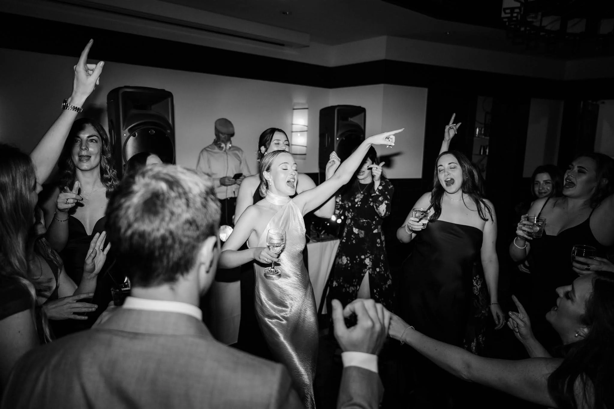 People dancing and celebrating at a party or wedding reception, with some holding drinks and enjoying music.