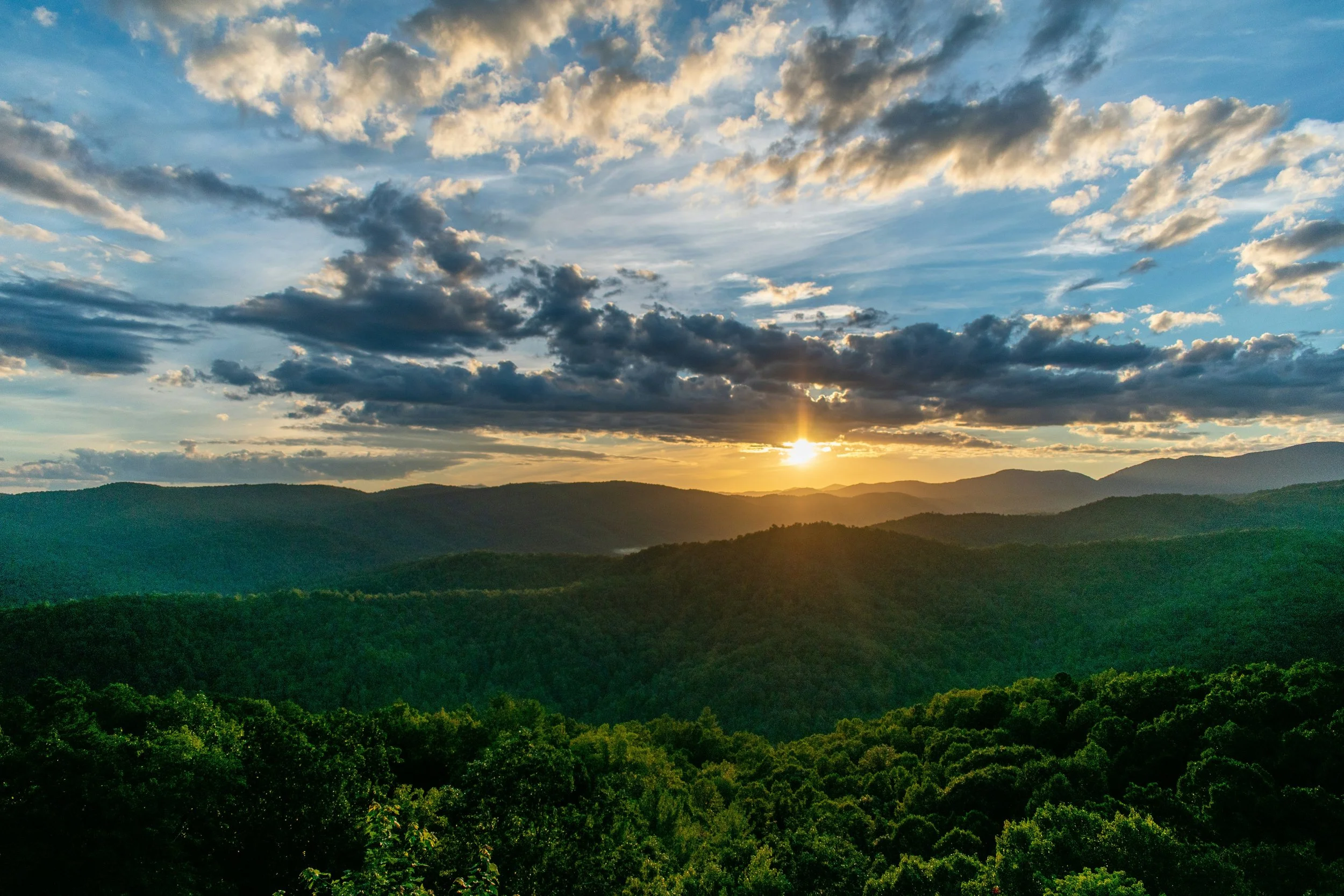 Sunset over a lush green mountain landscape with a partly cloudy sky.