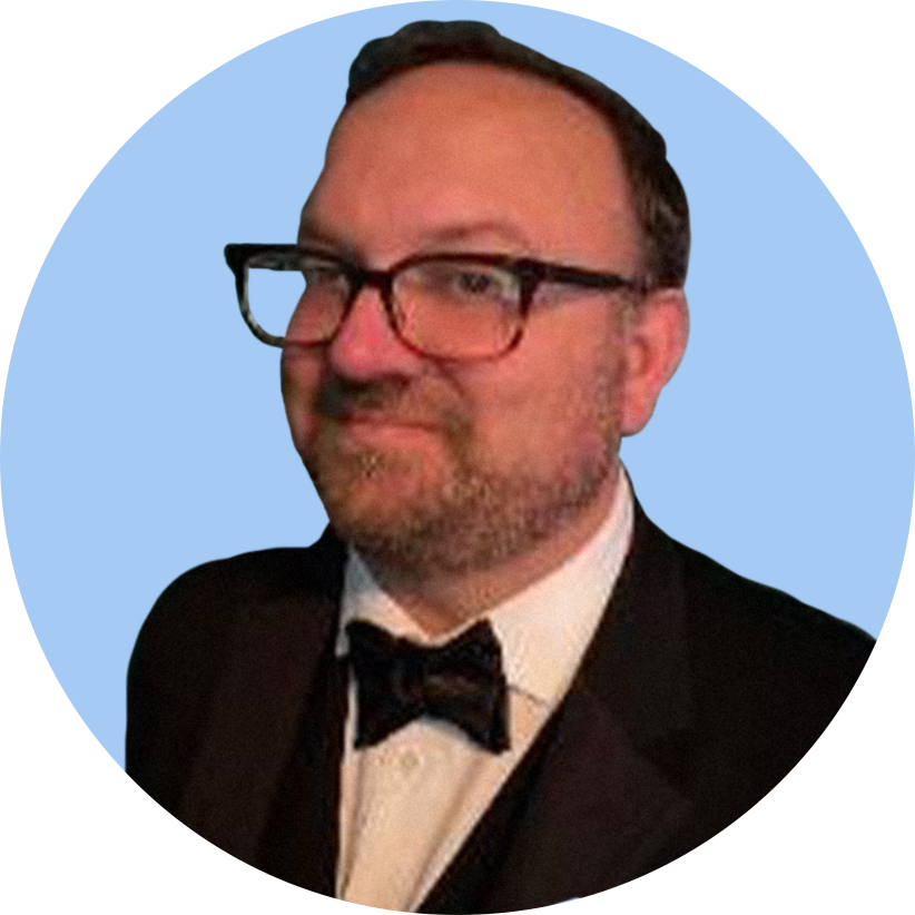 Portrait of a man dressed in a tuxedo with a bow tie, wearing glasses, against a light blue background.