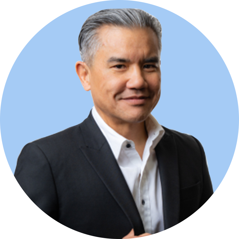 A professional man with gray hair in a dark suit and white shirt, smiling with a light blue background.