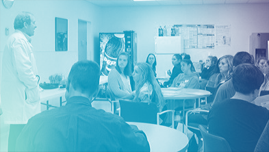 Group of people attending a meeting or presentation in a conference room with a speaker standing at the front.
