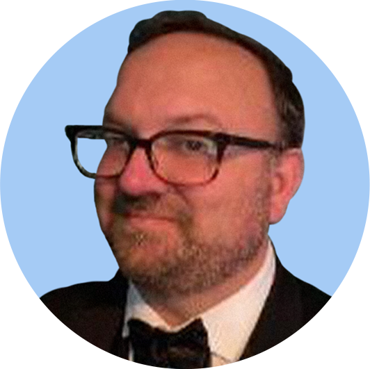 A man wearing glasses, a tuxedo, and a bow tie, with a light blue background.