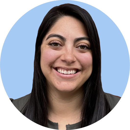 Close-up photo of a smiling woman with dark hair and light skin, wearing a gray shirt, against a light blue background.