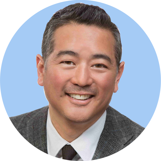 Smiling man in business attire with light blue background.