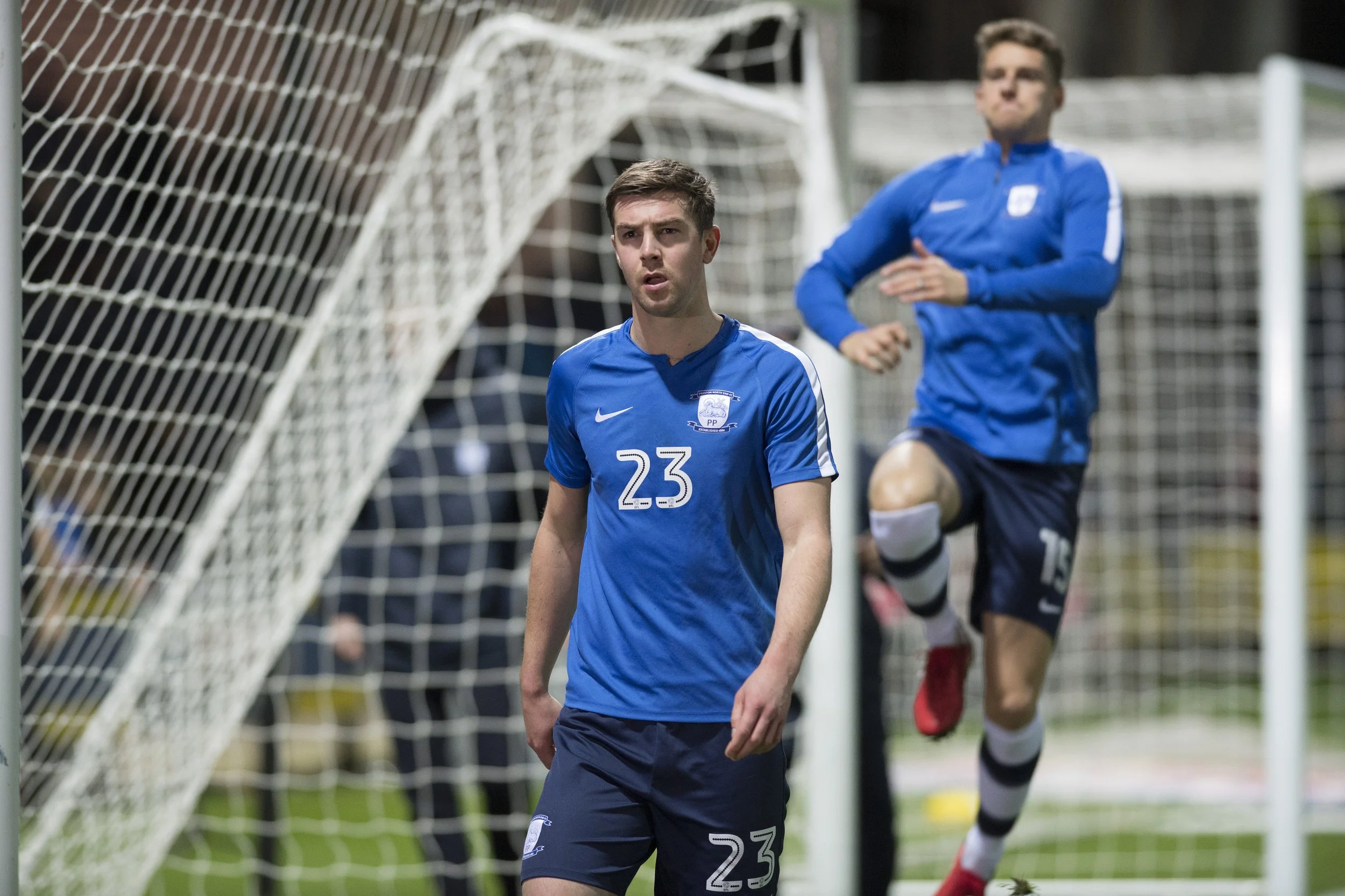 Soccer players in blue jerseys warming up or practicing near a goal post on the field.