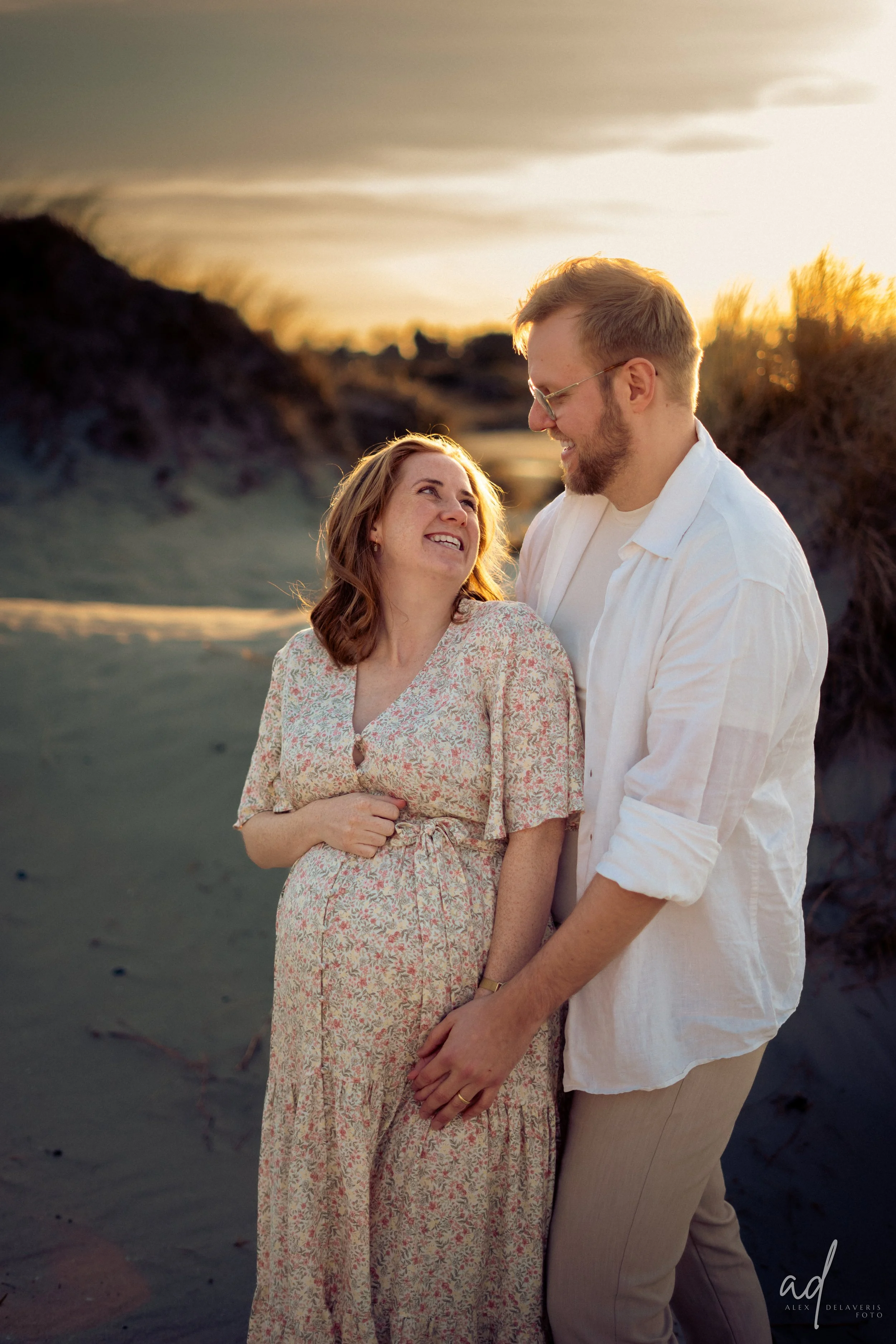 A couple smiling and looking at each other on a beach during sunset.