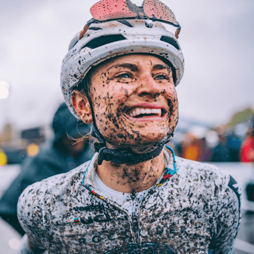 Three people having a conversation in an office with large windows, two of them are holding coffee mugs, and one person is standing by the window.