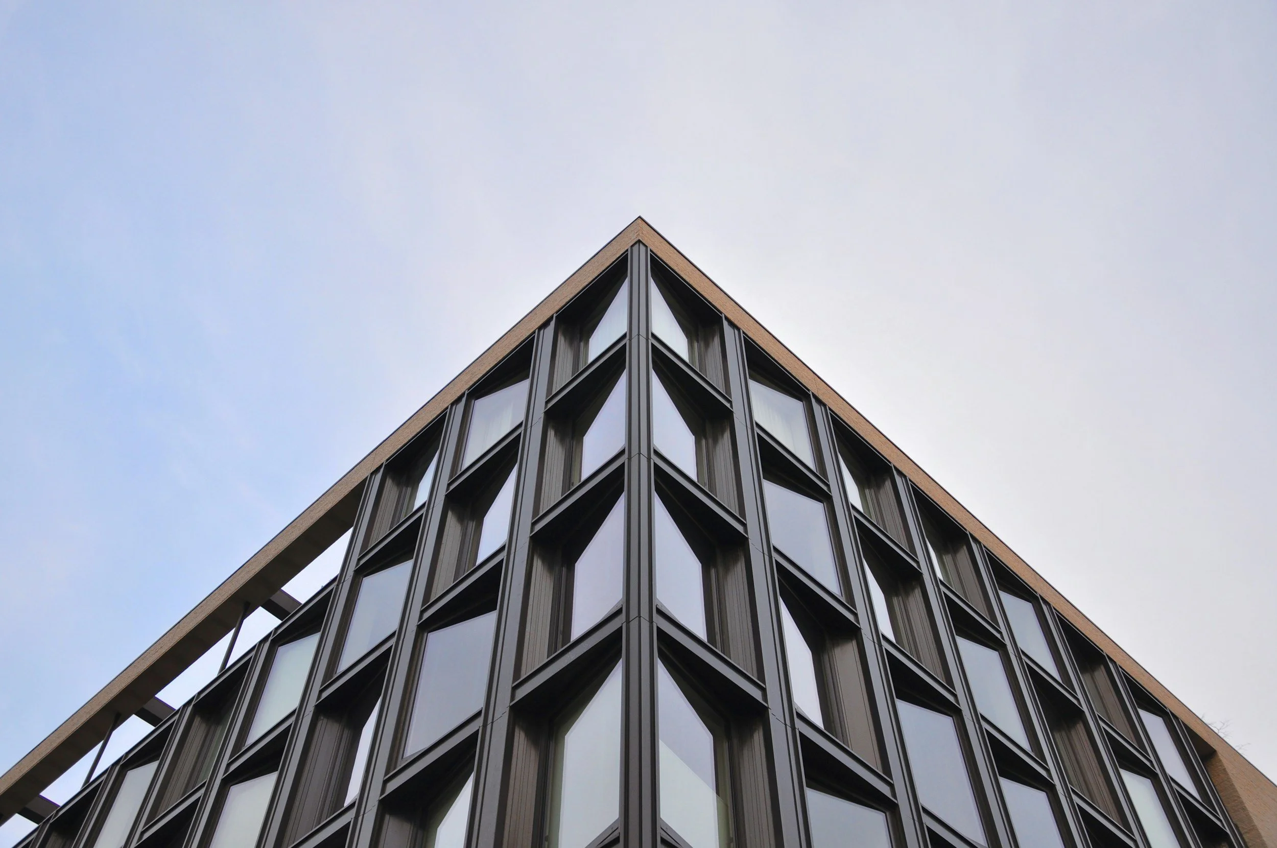 Low-angle view of a building corner featuring sharply angled windows and an exposed metal structural frame, emphasizing architectural form and feasibility considerations.