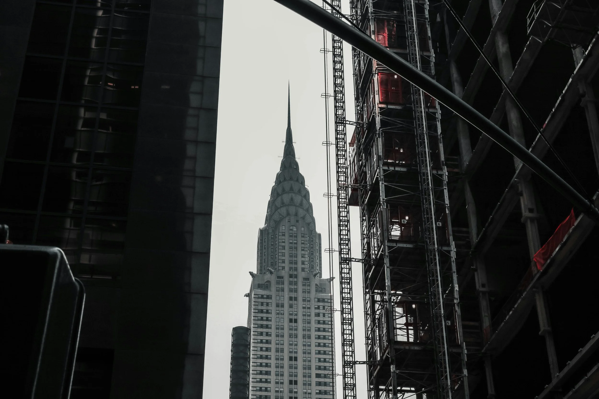 Image of the Chrysler Building framed between modern steel construction scaffolding and adjacent high-rise structures.