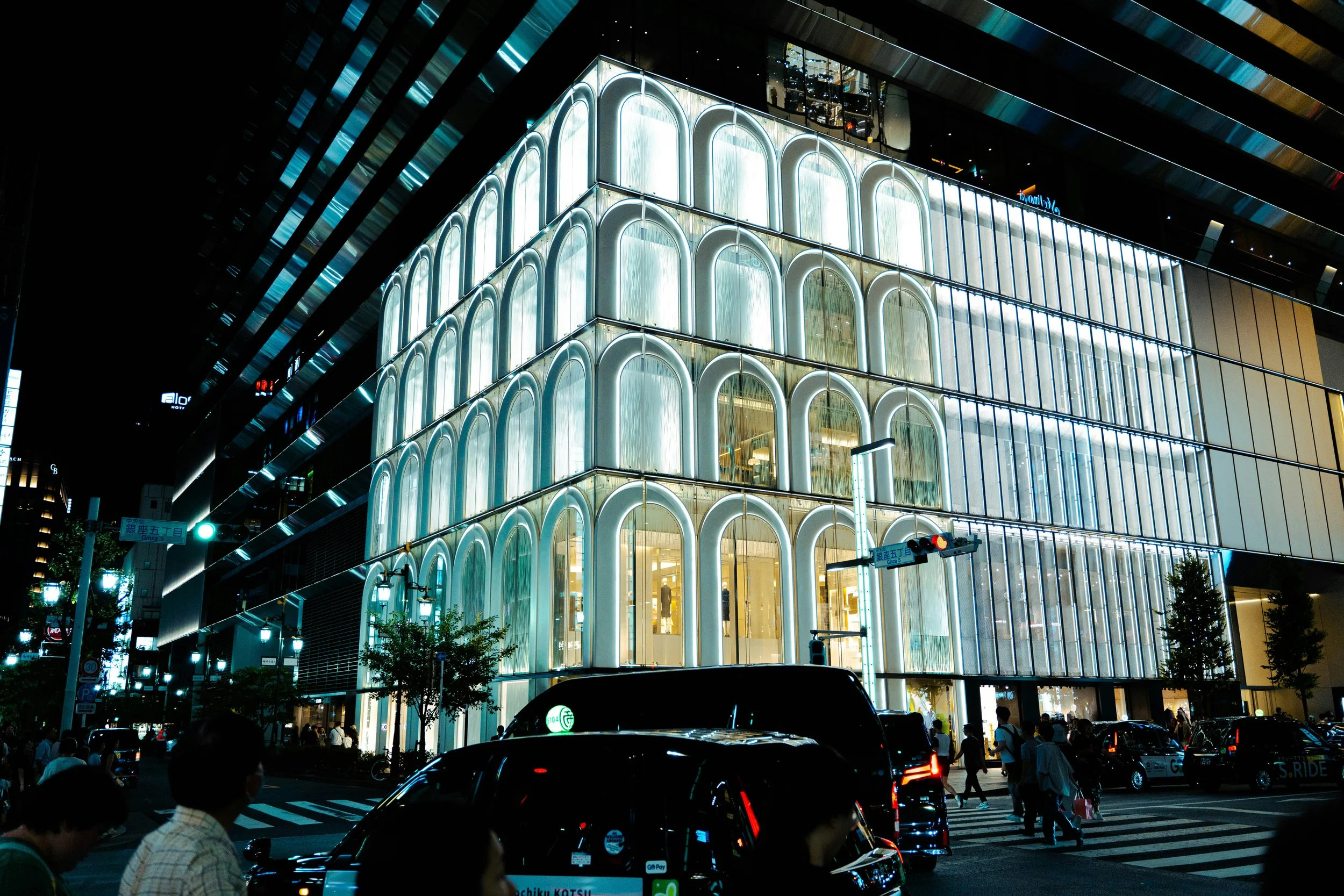Nighttime view of a multi-story glass building featuring illuminated arched façades and a transparent structural framework that highlights contemporary engineering and façade design.