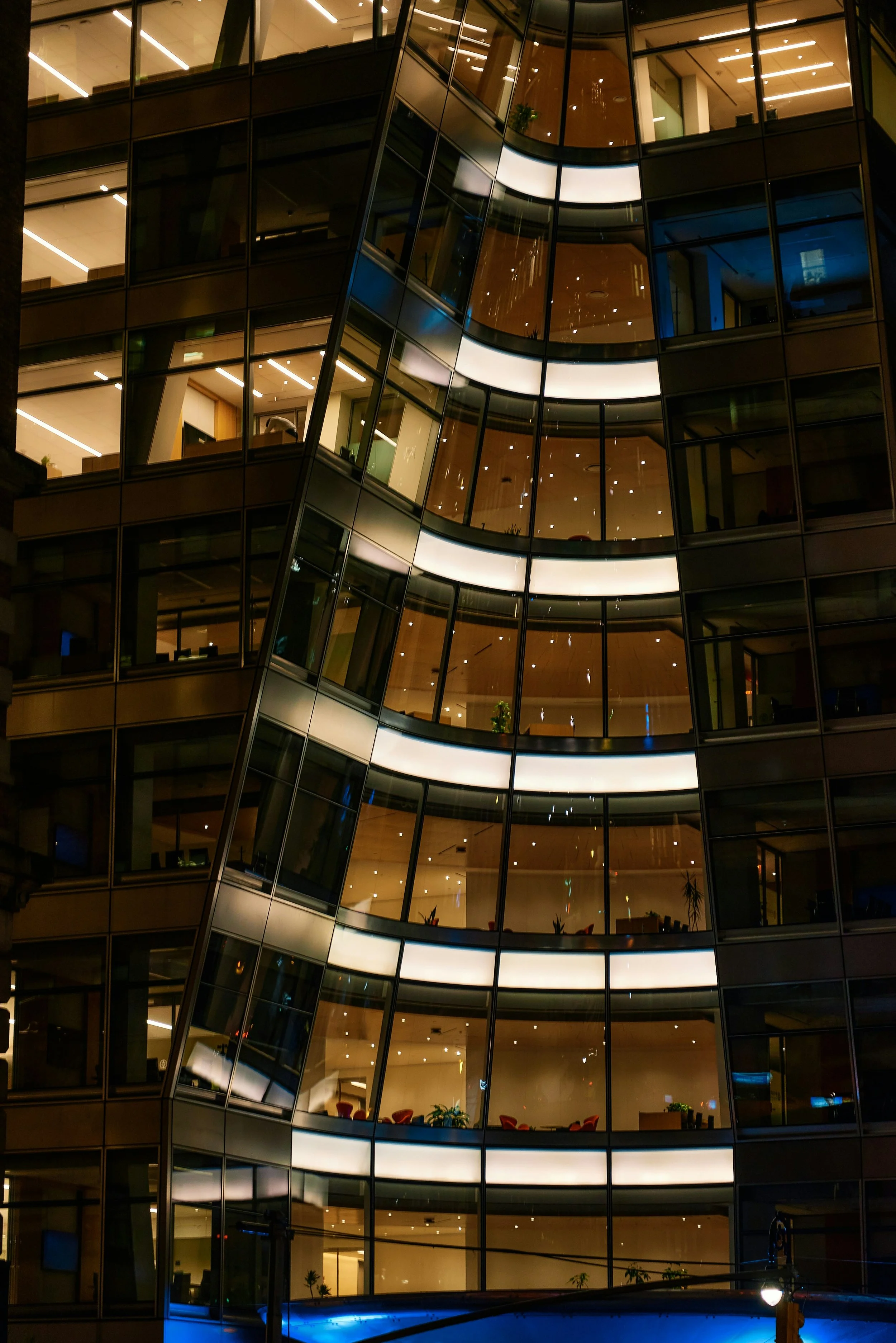 Exterior nighttime view of a modern building with a glass and metal façade illuminated by interior and architectural lighting.