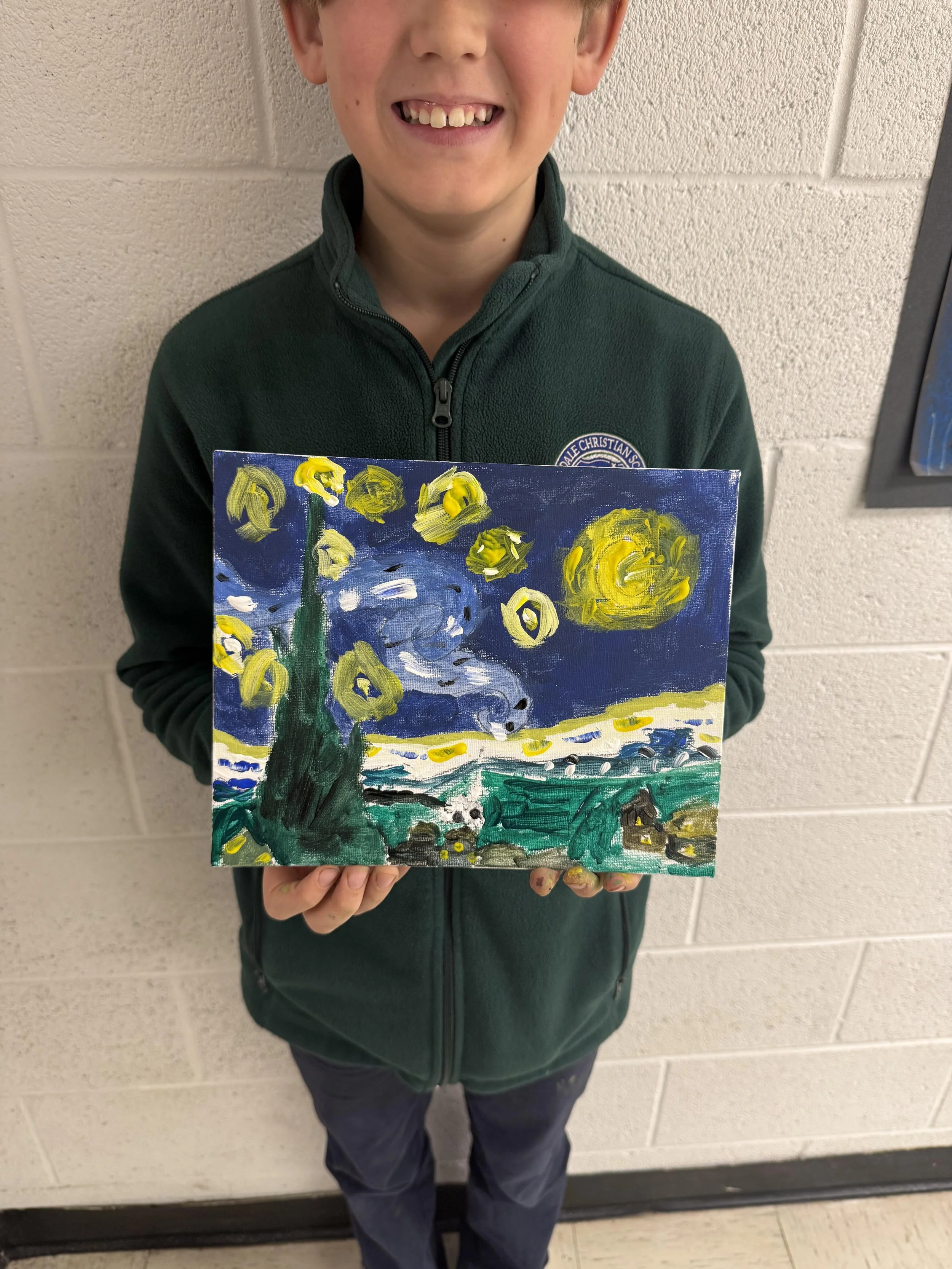 A young boy in a green zip-up jacket is holding a painting of Vincent van Gogh's Starry Night. The painting features swirling night sky with yellow stars and a bright moon, a dark cypress tree, and a countryside landscape.