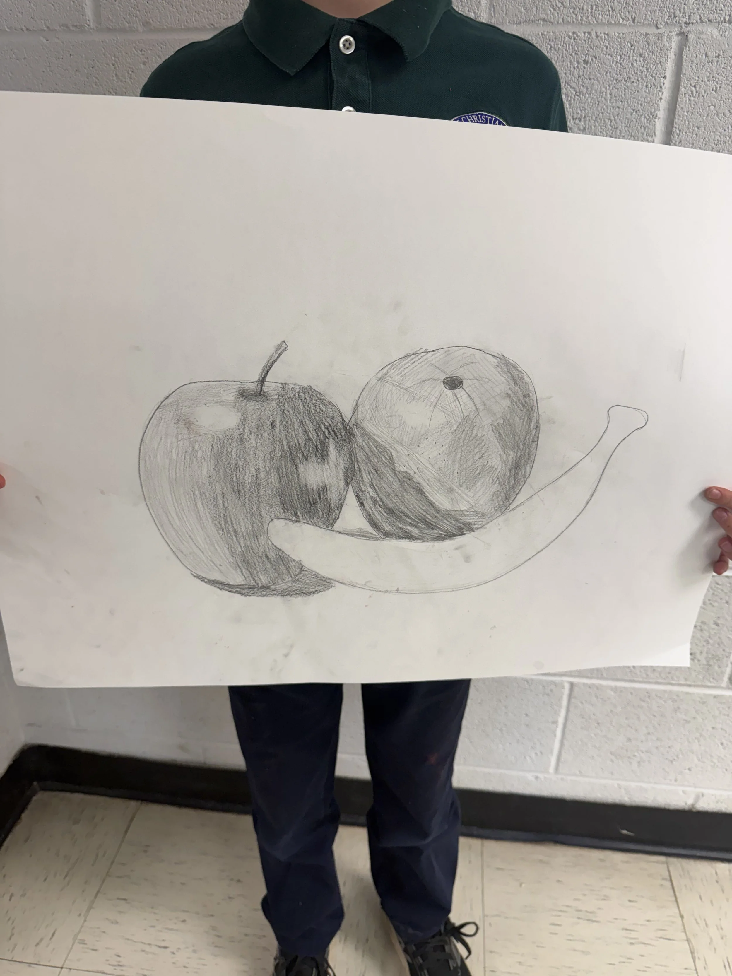 Child holding a large drawing of an apple, a pear, and an apple on white paper.