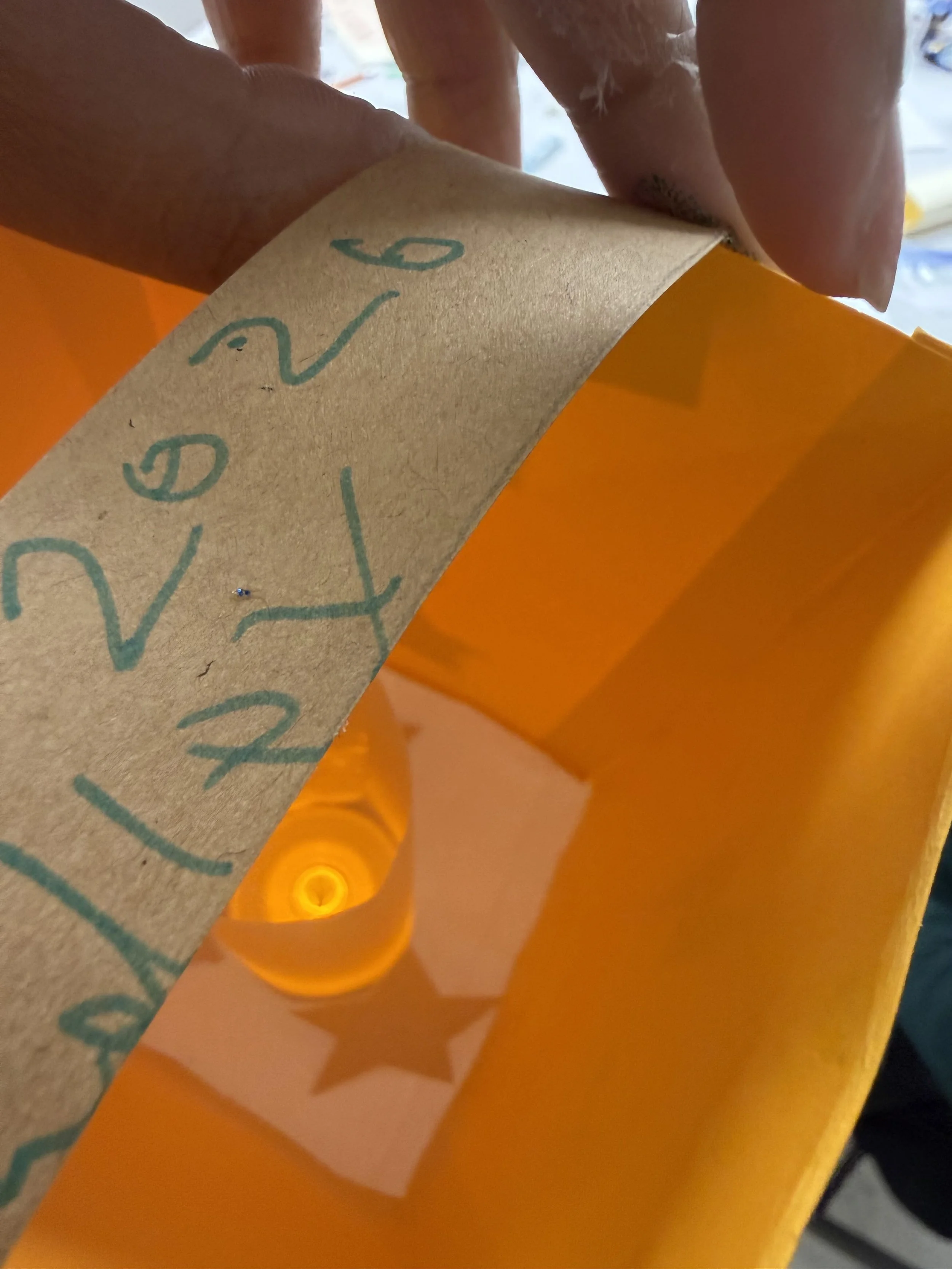 Close-up of a yellow paper bag with a brown paper strip that has handwritten text. Inside the bag, a lightbulb with a star reflection is visible.