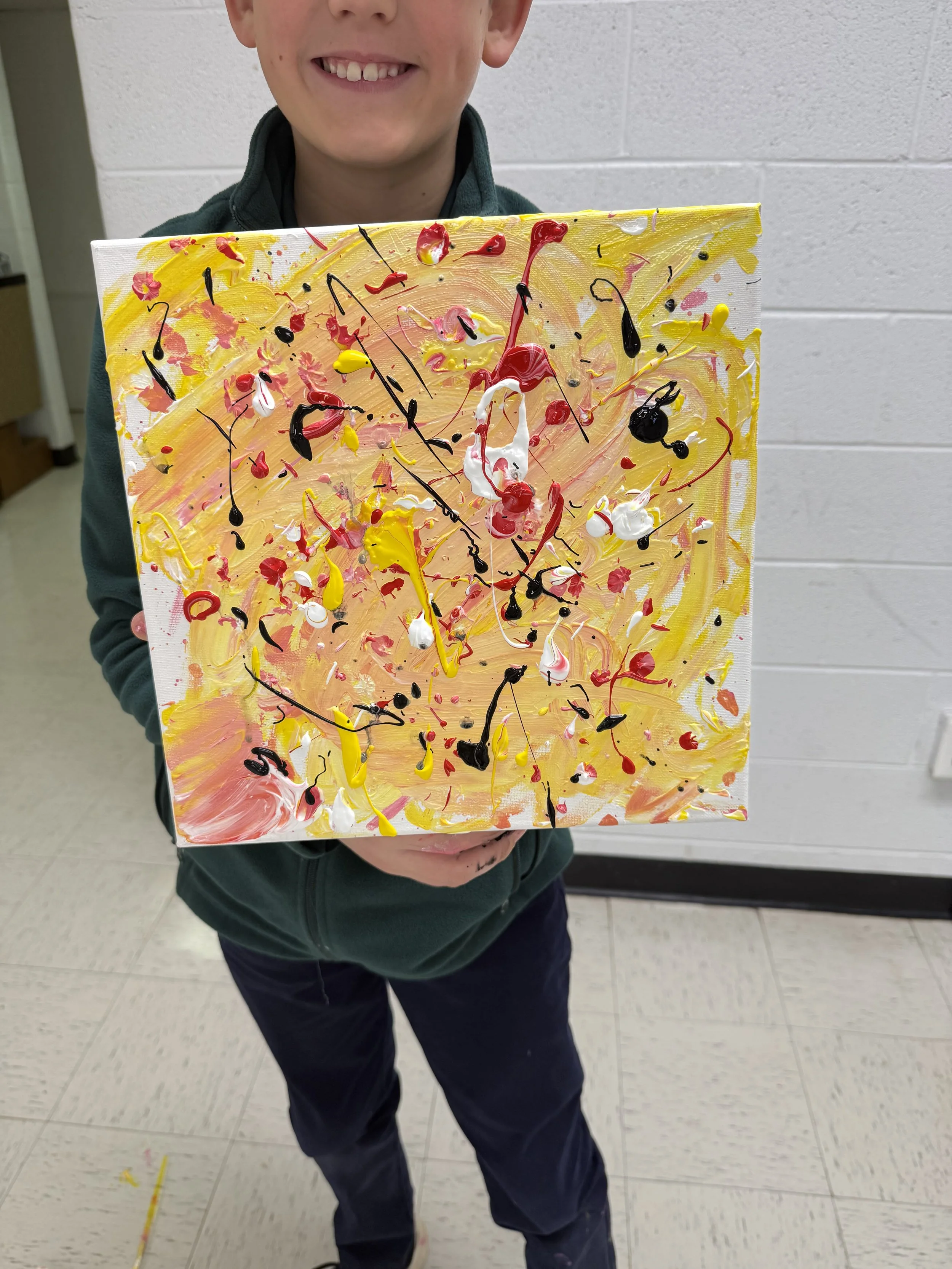Smiling boy holding a colorful abstract painting with yellow, red, black, white, and pink splatters and swirls.