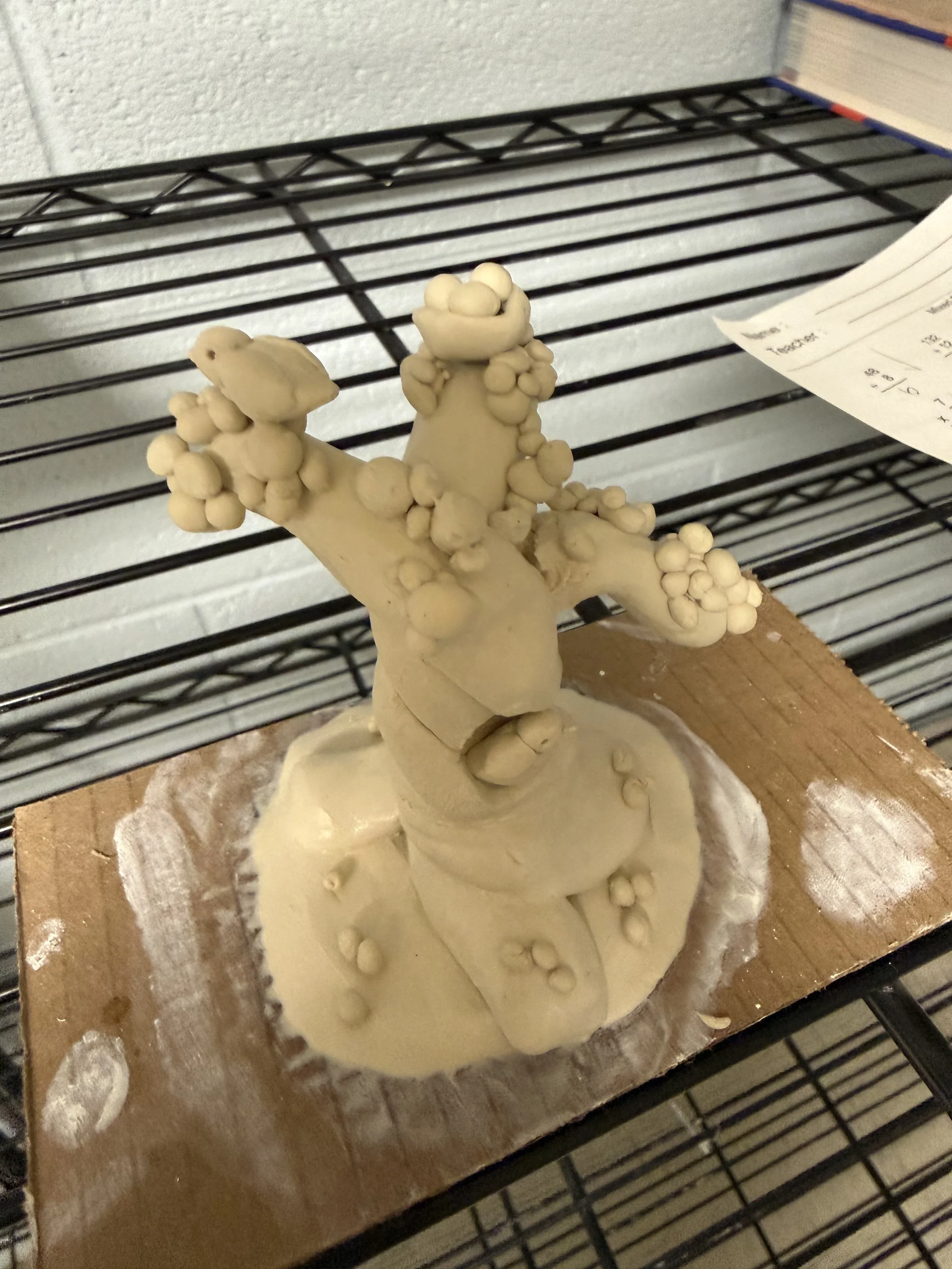 Clay sculpture of a tree with multiple rounded branches on a wooden base.