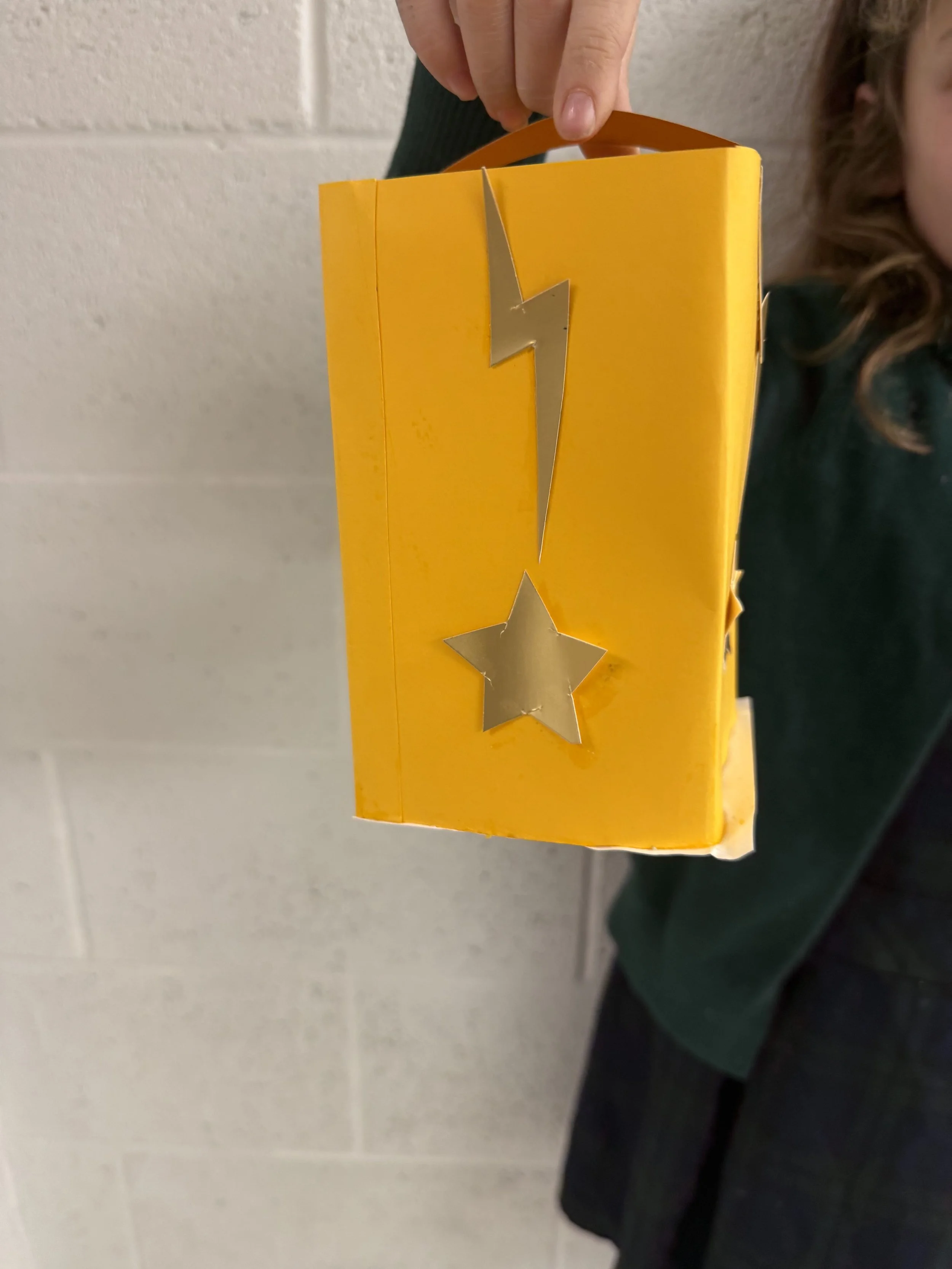 A person holding a yellow box decorated with a silver lightning bolt and star on the front.
