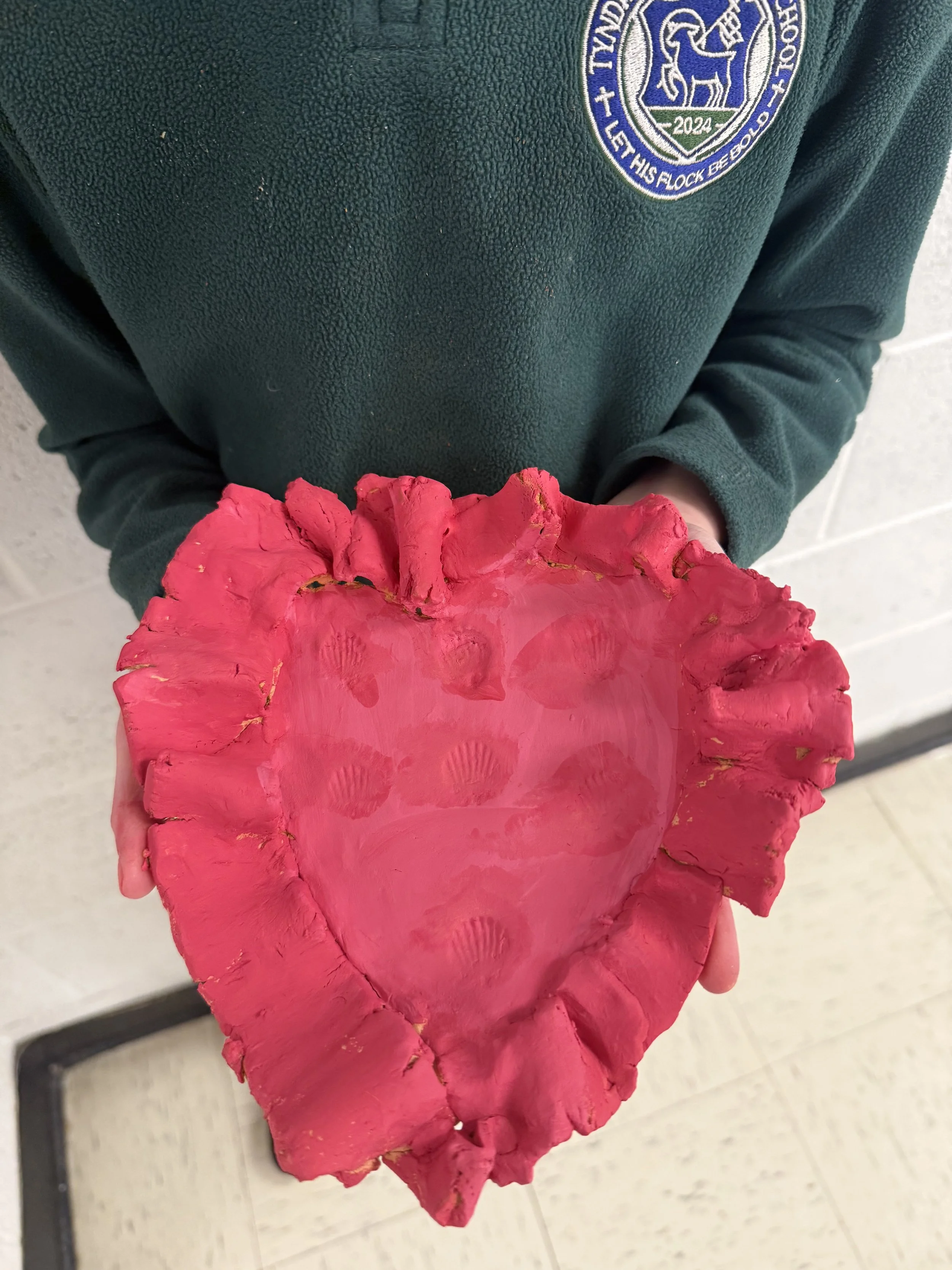 Person holding a large, pink, heart-shaped object with a rough, textured surface.