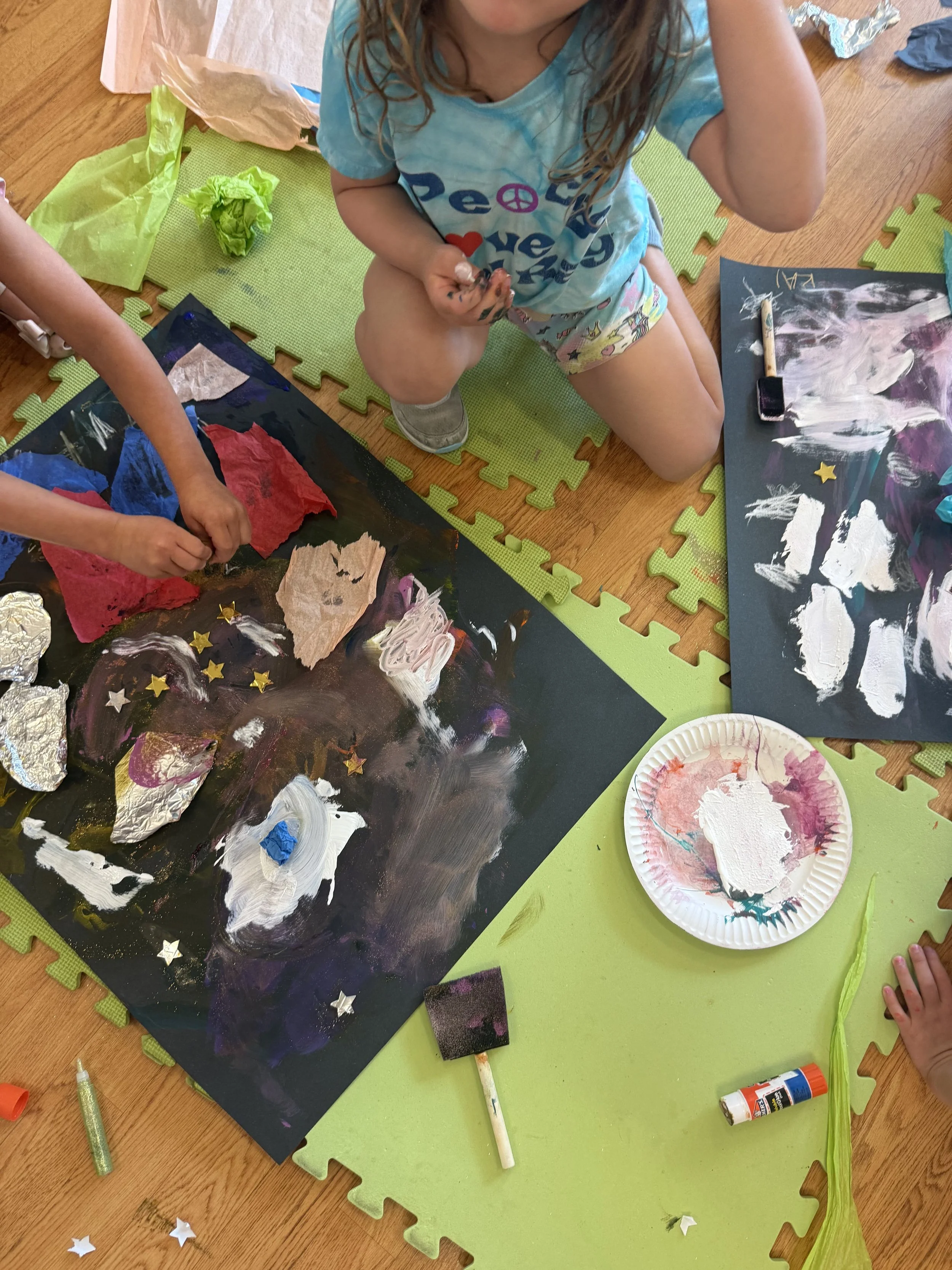 Children creating a colorful galaxy-themed art project with metallic and star-shaped decorations on black paper.