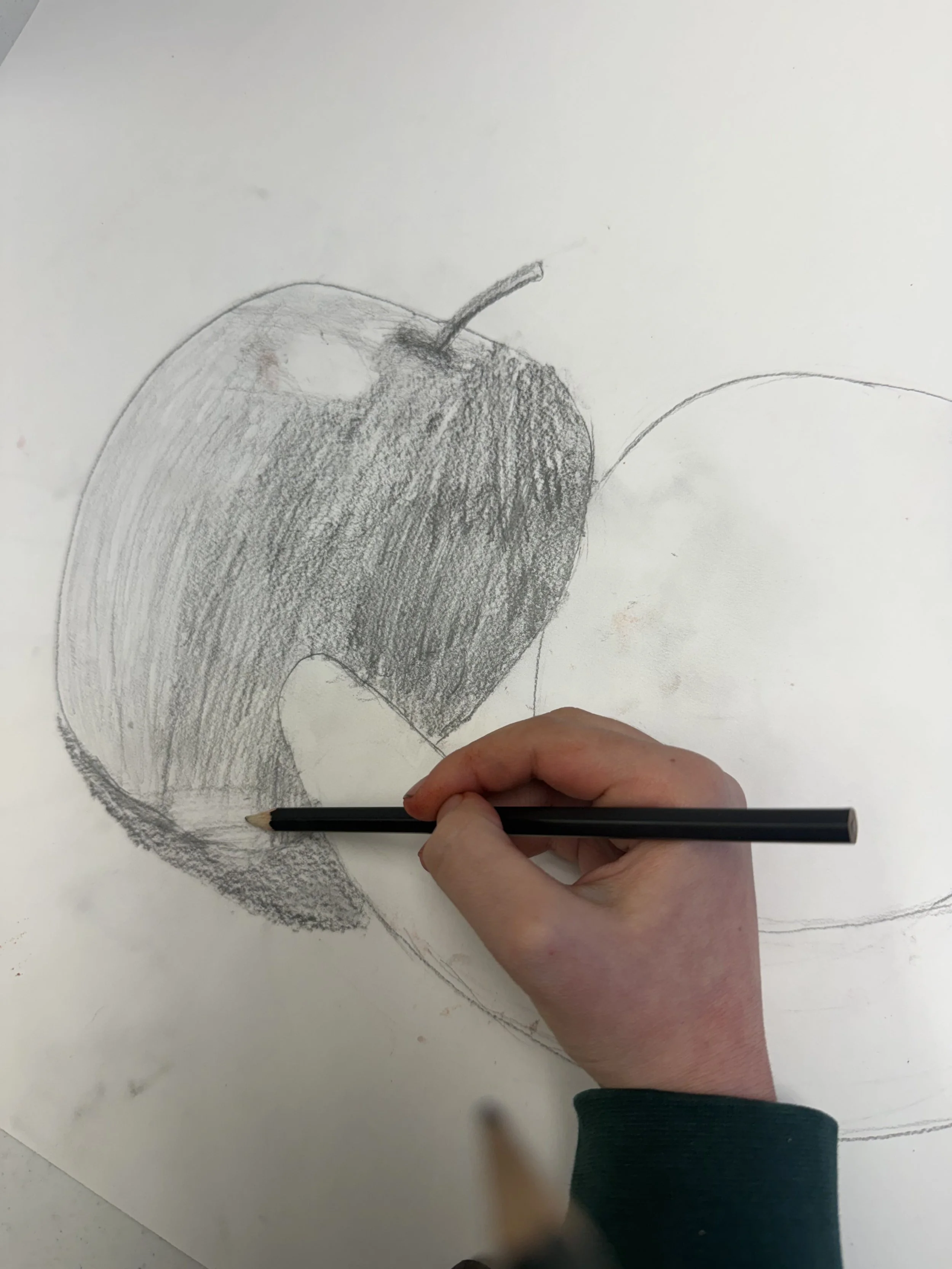 A hand sketching an apple on a white piece of paper with a pencil.