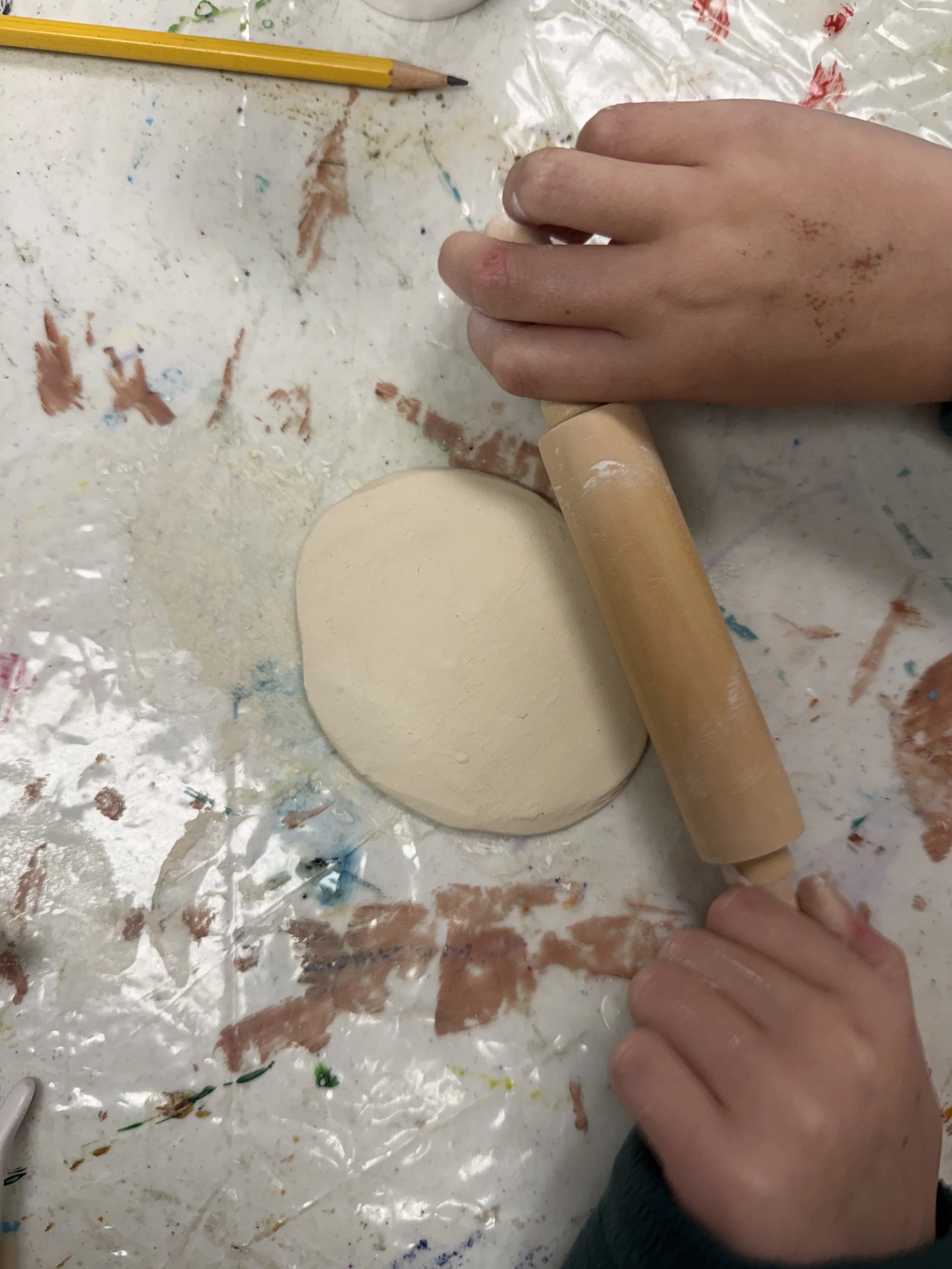 Child rolling out clay with a rolling pin on a messy surface.