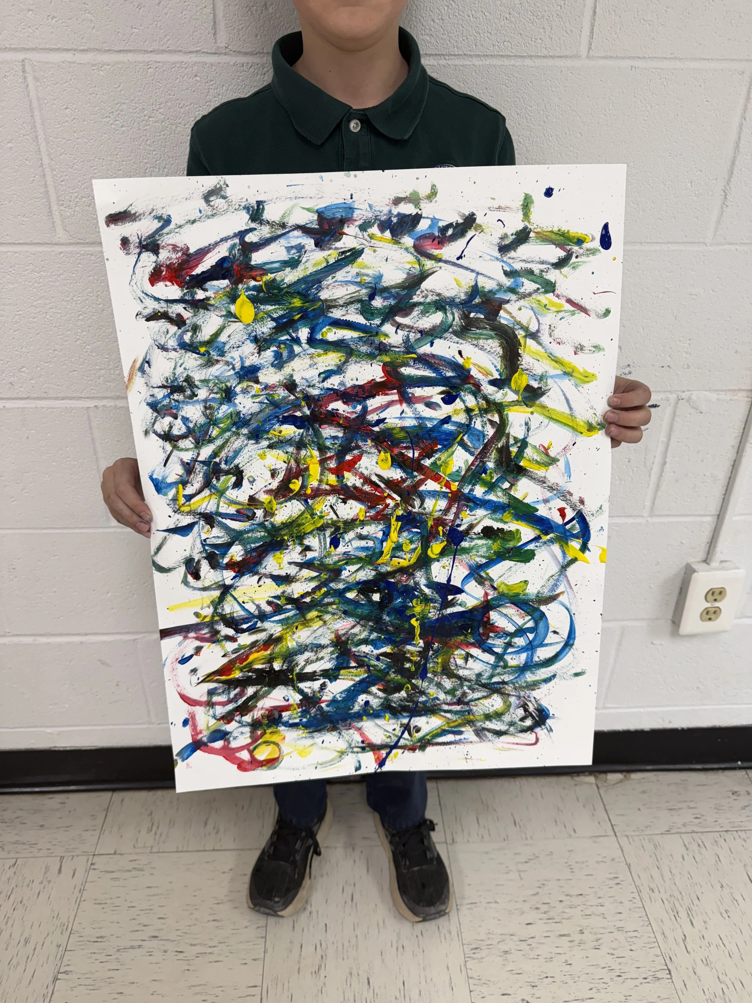 Child holding colorful abstract painting with splashes of blue, yellow, red, green, and black.