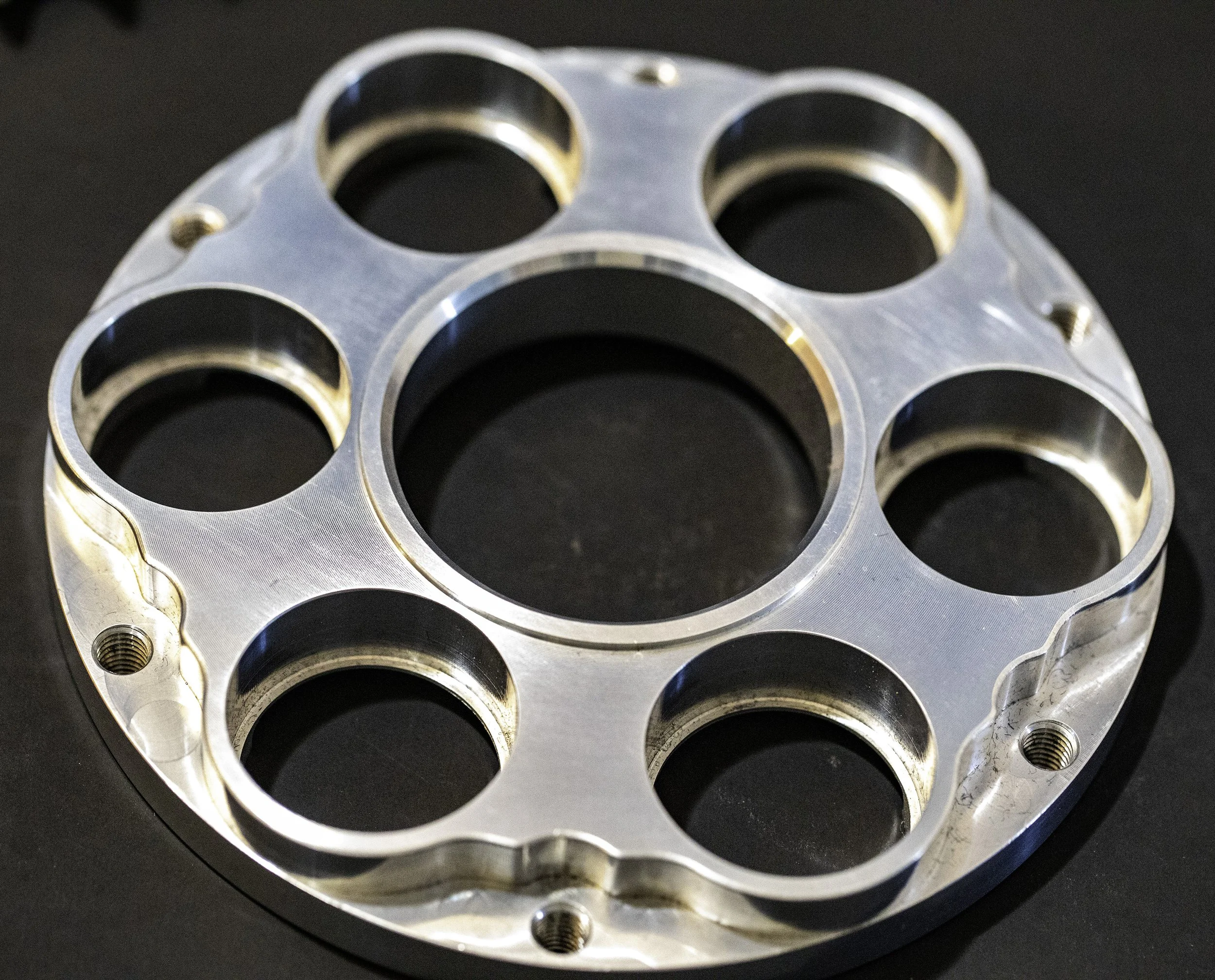A round, metallic component with multiple circular holes and threaded screw holes, A Ducati carrier