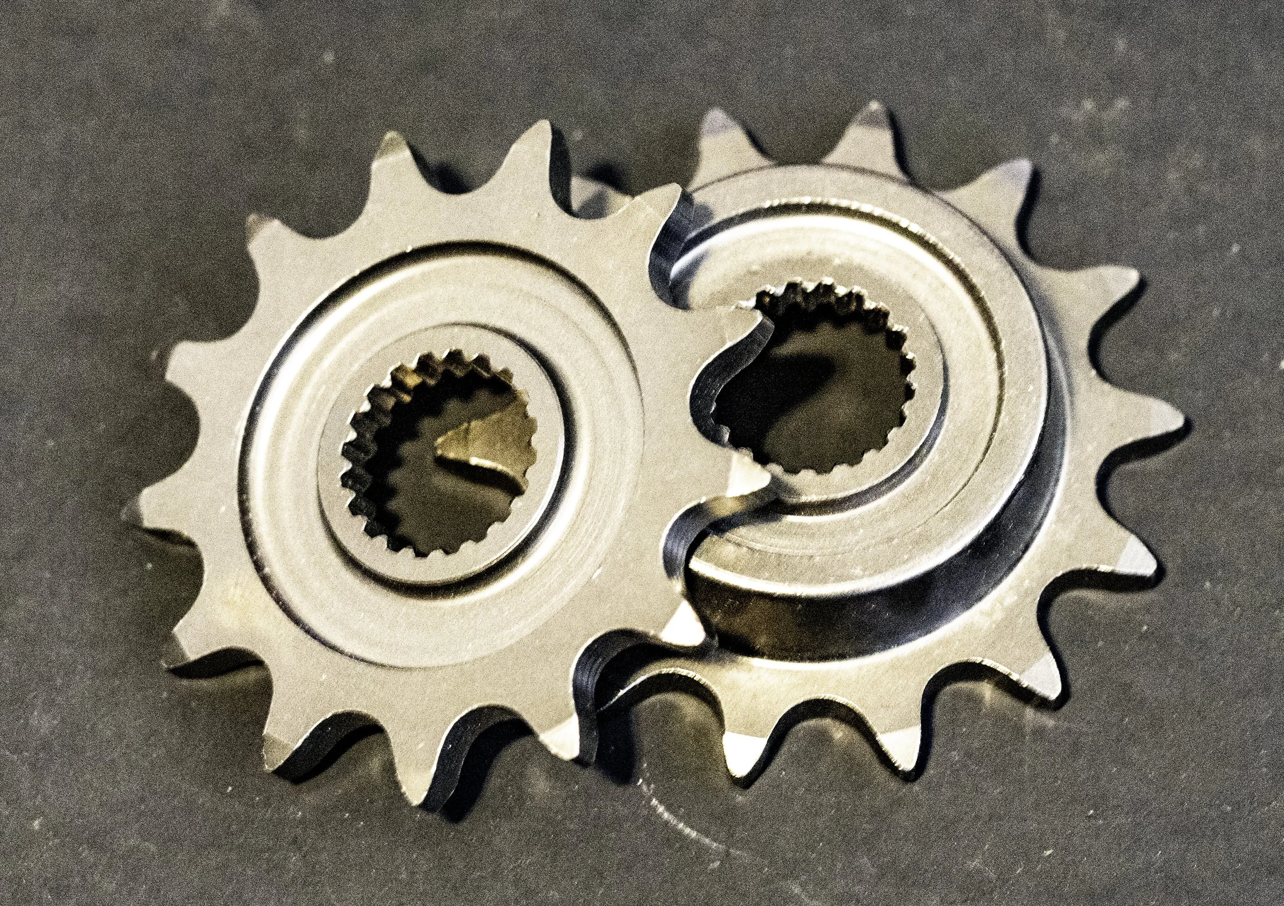 Two metal motorcycle sprockets a dark background.