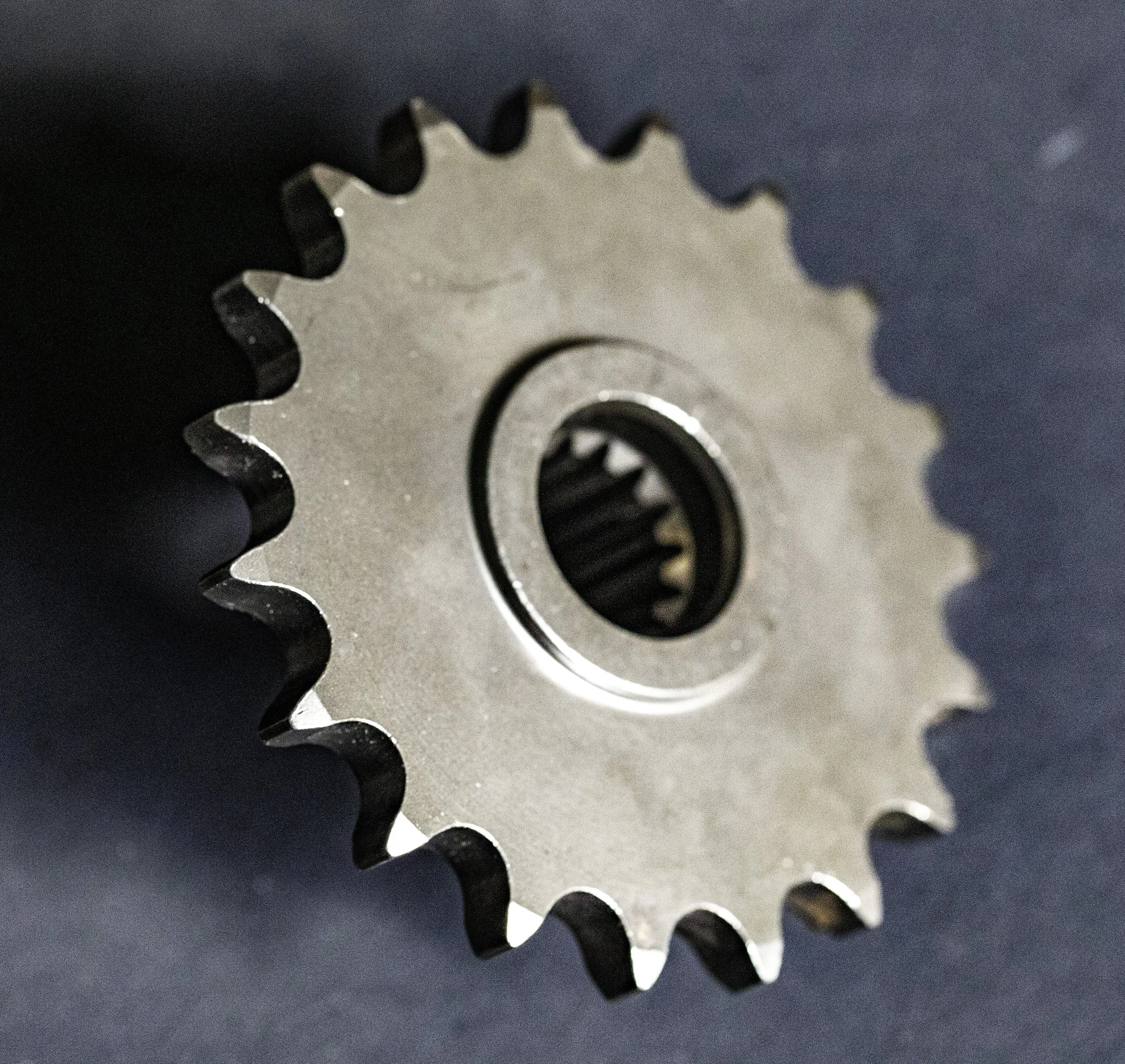 Close-up of a metallic sprocket or gear with evenly spaced teeth, set against a dark background.