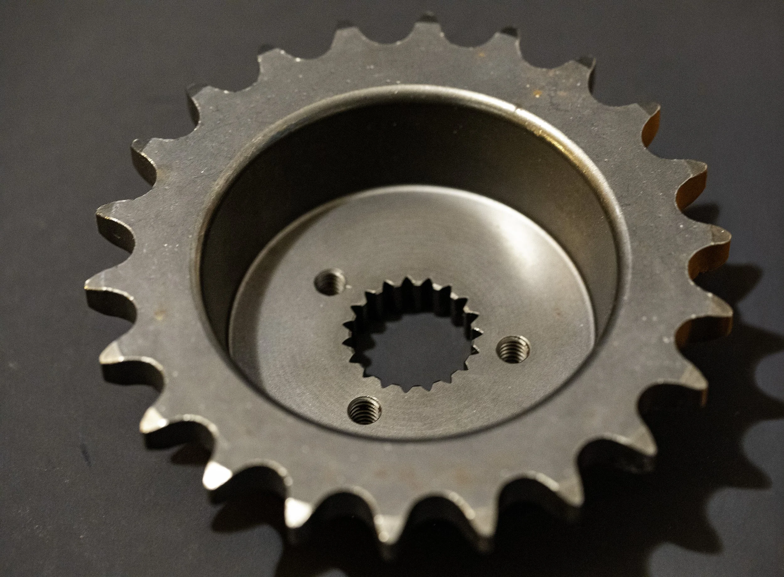 A metal sprocket with teeth, viewed from above, on a dark surface. Harley Davidson