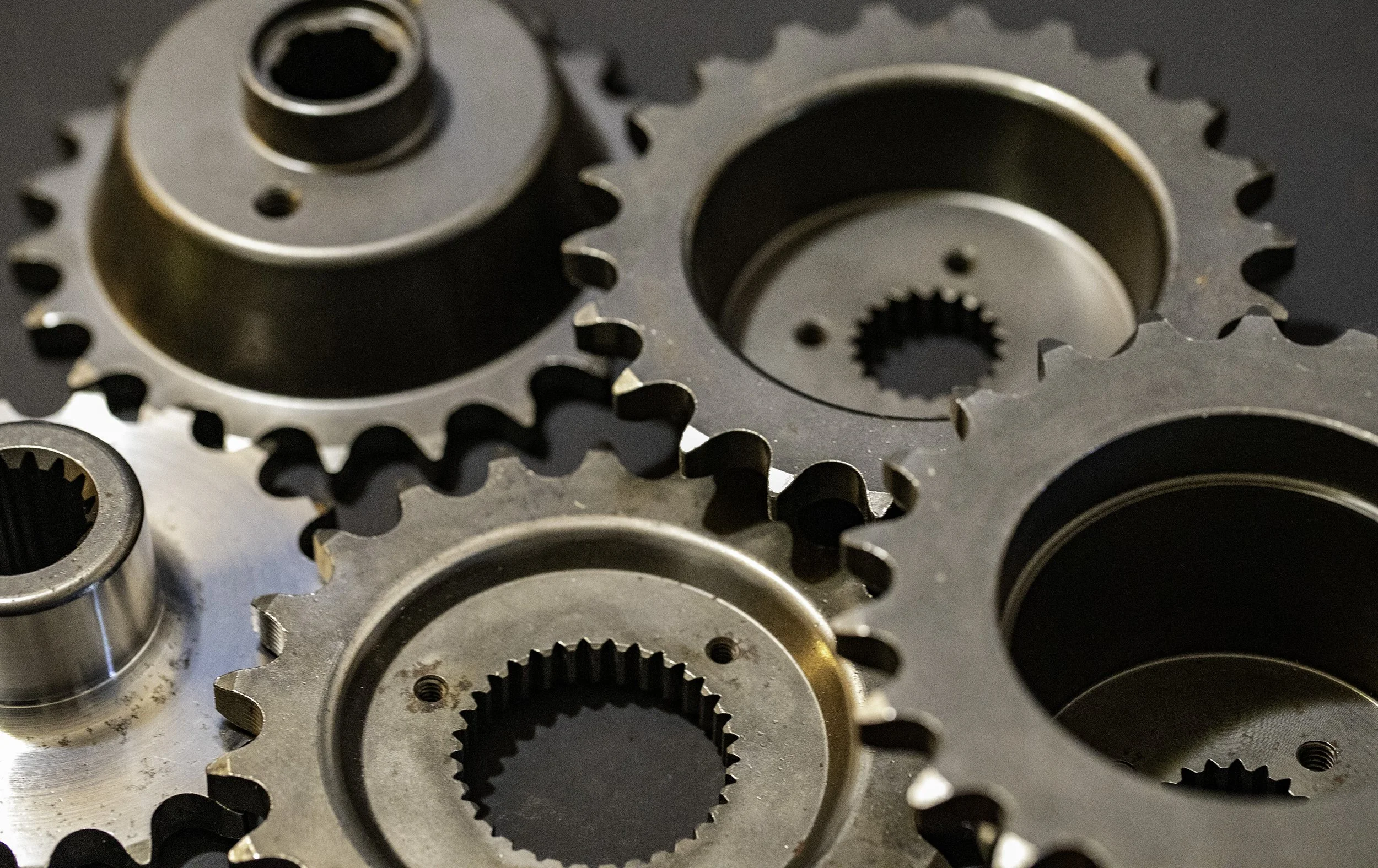 Close-up of assorted metallic sprockets with gear teeth and central holes, some with internal splines. For Harley Davidson