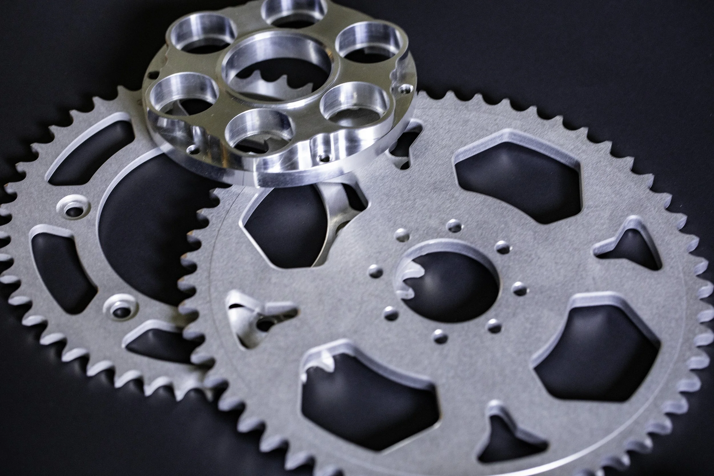 Close-up of metallic motorcycle sprockets  placed on a black surface.