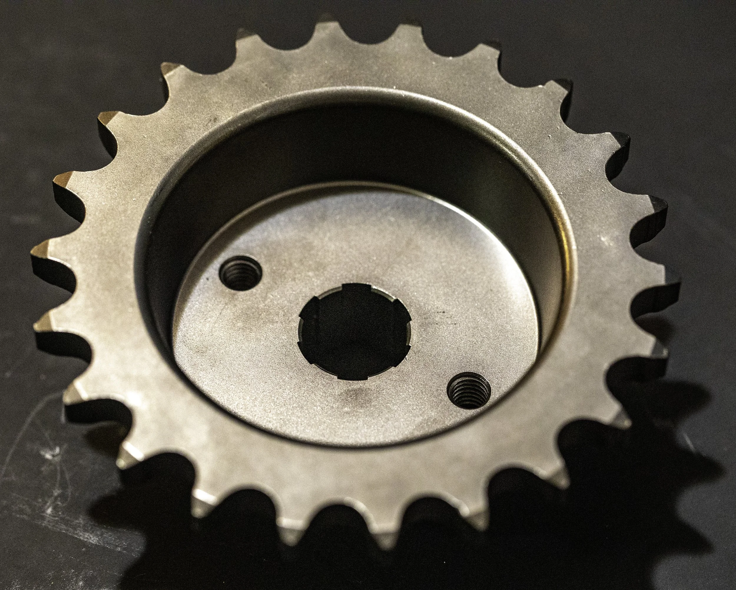 Close-up of a metal sprocket with evenly spaced teeth, placed on a dark surface. Harley Davidson