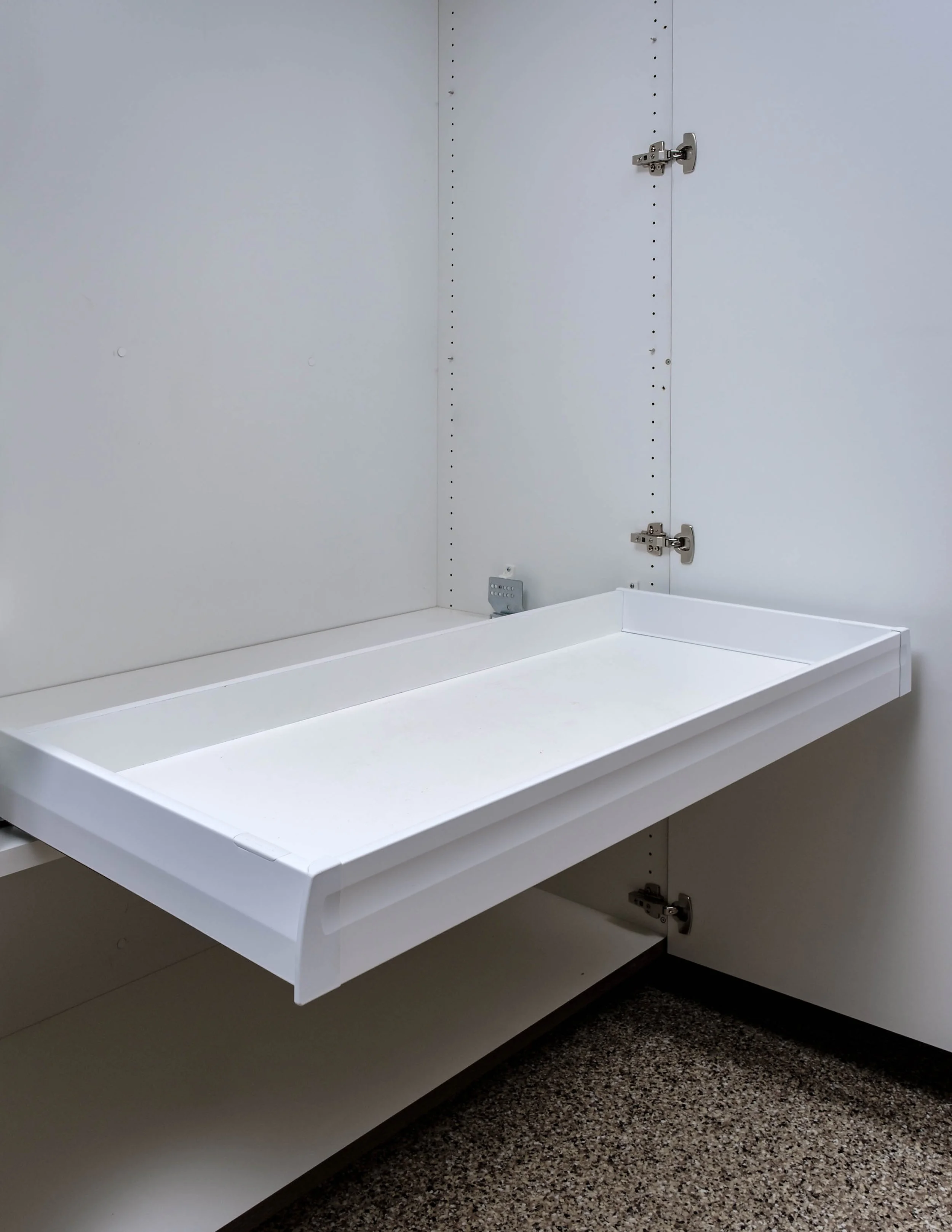 Empty white shelf inside a white cabinet with adjustable hinges in a room with brown speckled carpet.
